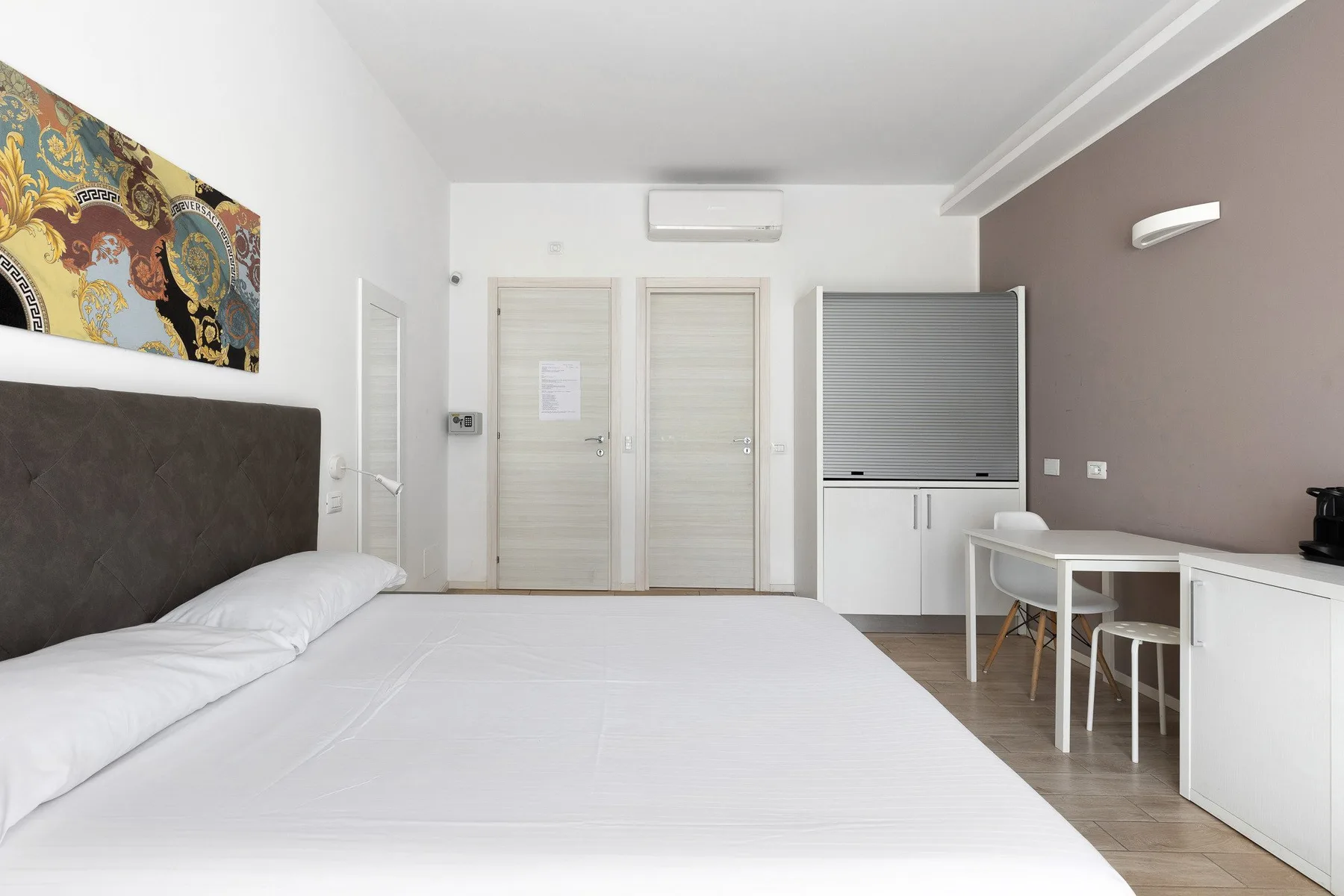 A bright bedroom with a large bed, wall-mounted air conditioner, and small dining table.