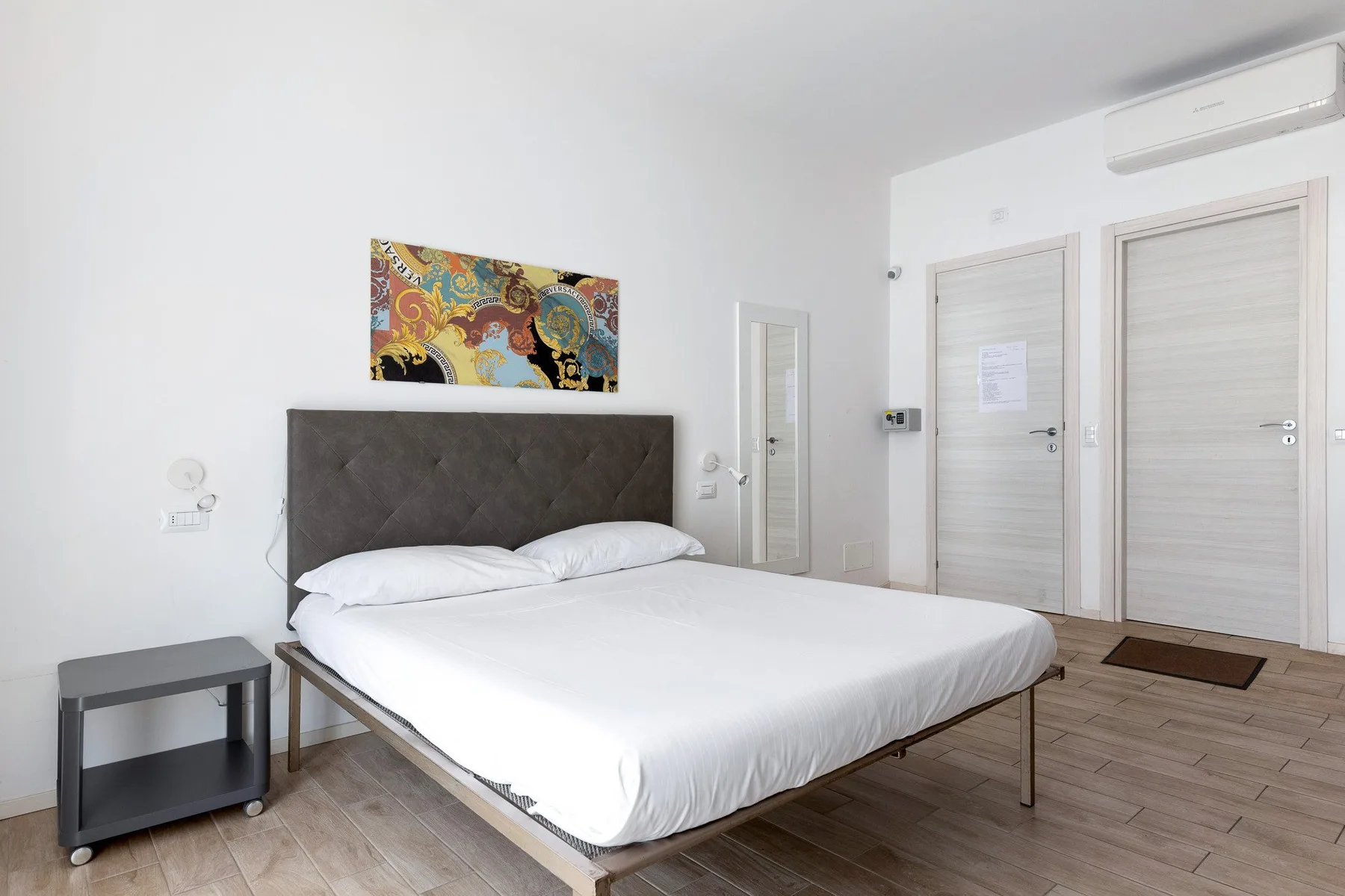 A bright bedroom with a neatly made bed and colorful artwork above the headboard.