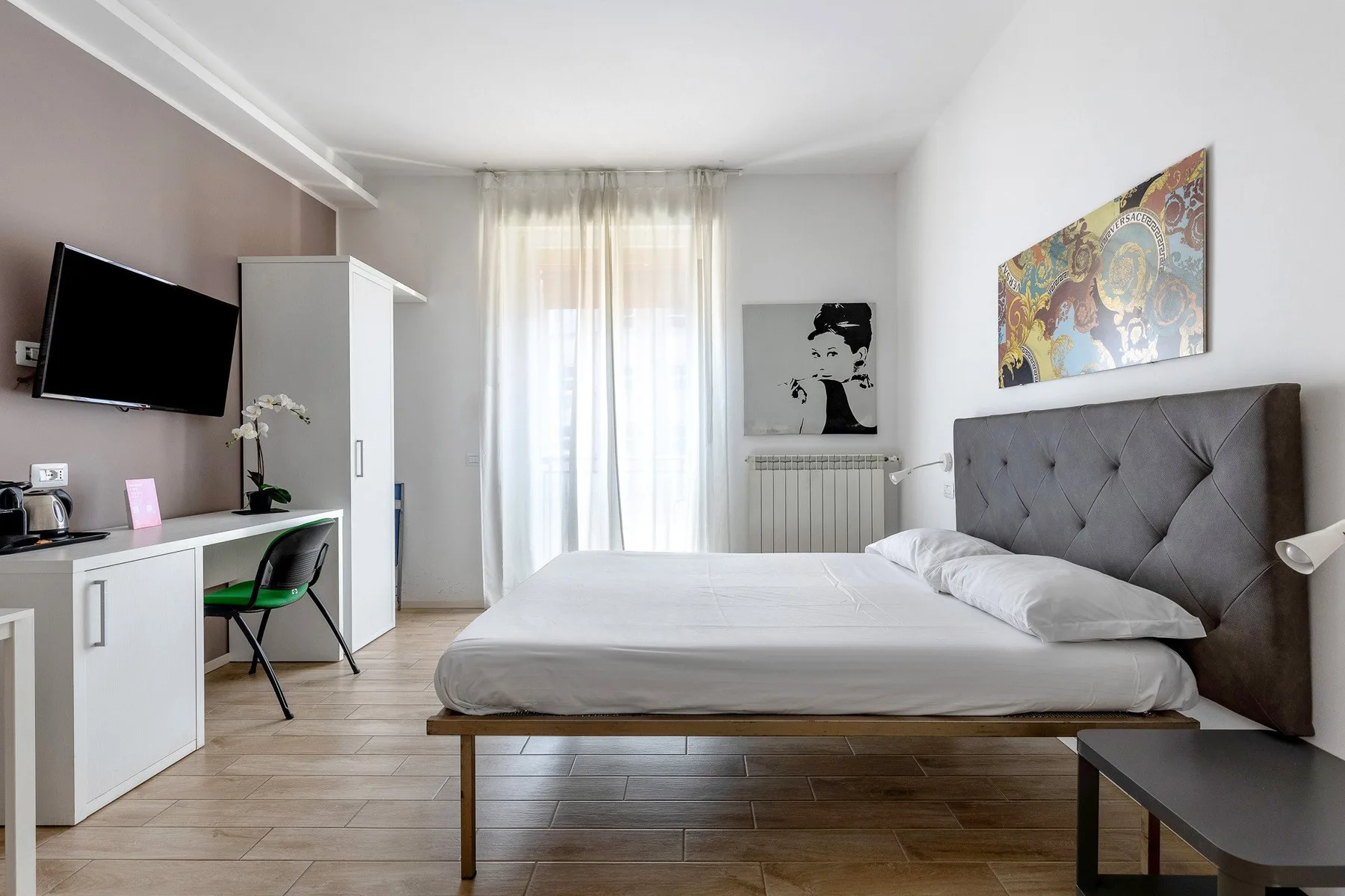 Un dormitorio luminoso con una cama, un escritorio y cortinas translúcidas en la ventana.
