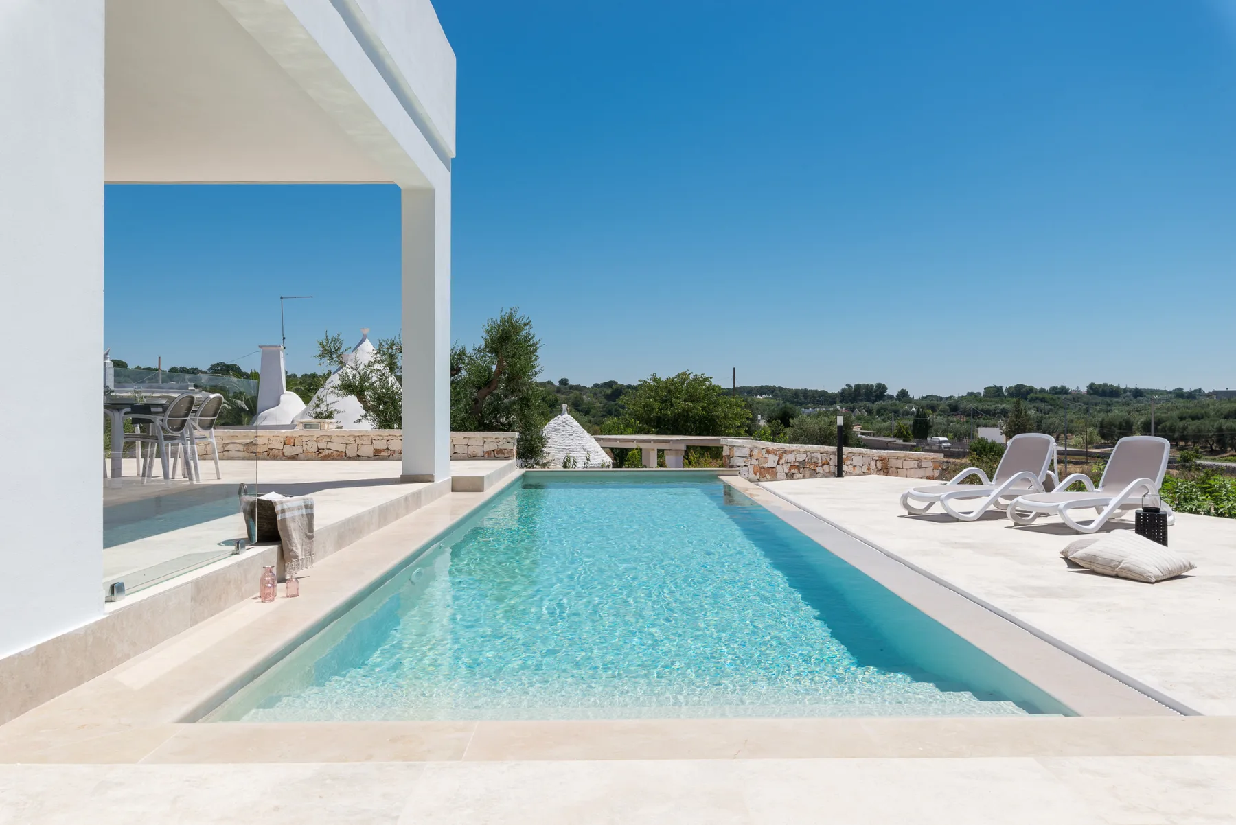 A swimming pool beside a terrace with lounge seating and a sunny open view.