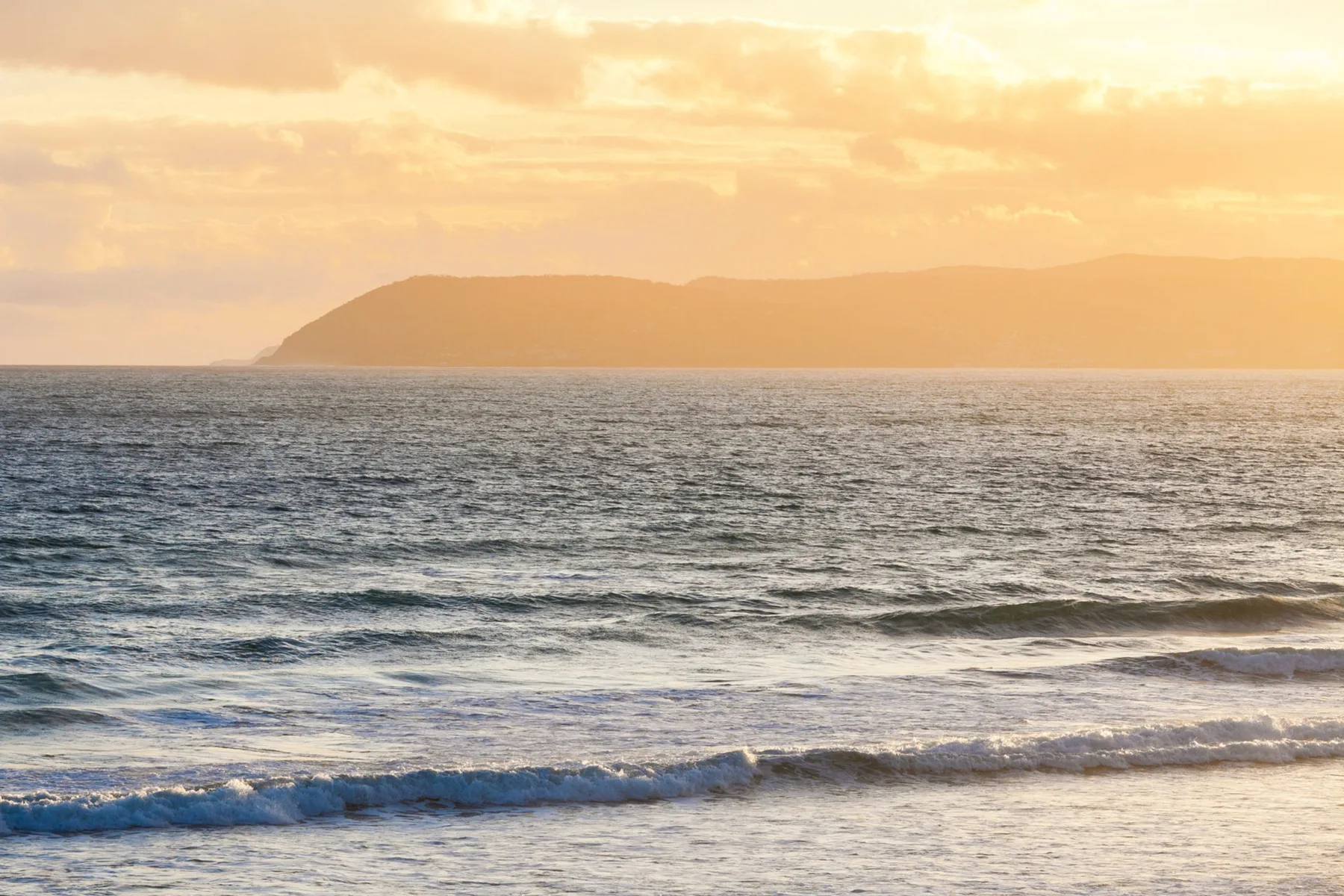 Ocean waves roll toward the shore beneath a hazy sunset sky.