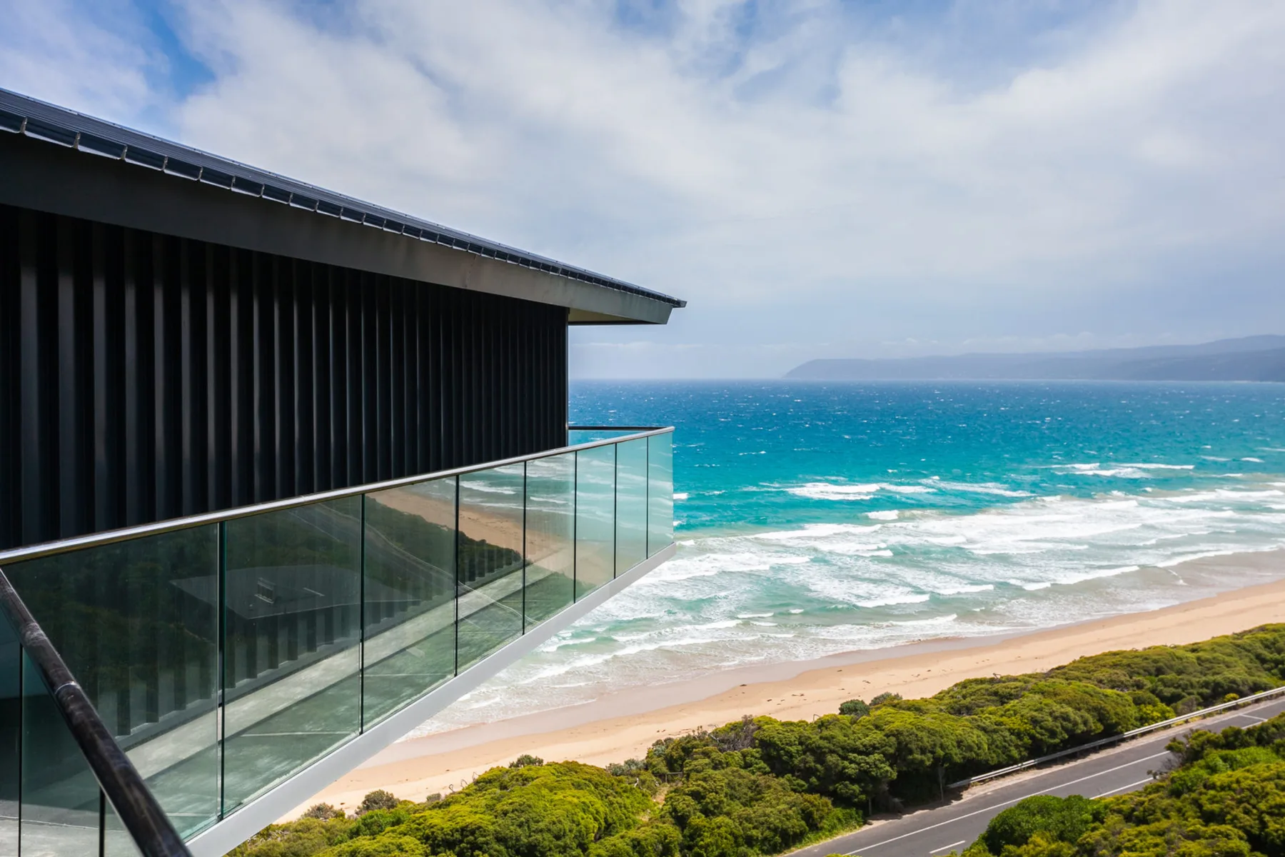A modern house overlooks a sandy beach and blue ocean.