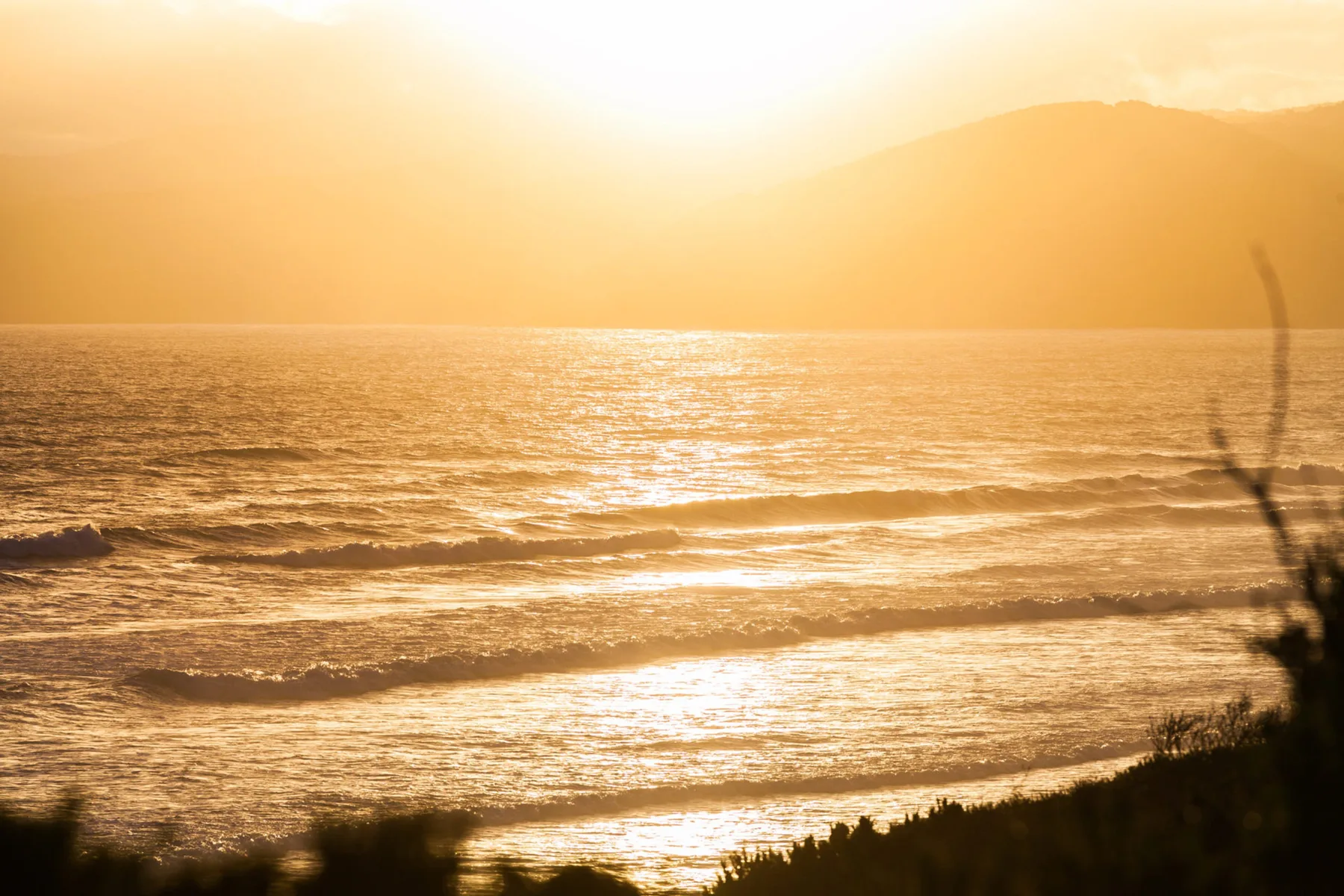 Sunset over the ocean, with waves breaking along the shore.