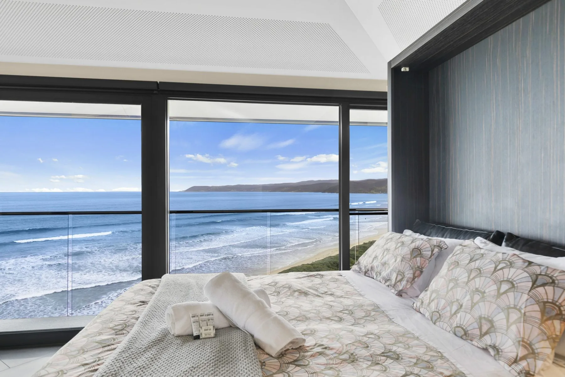 A bedroom with a bed beside large windows overlooking the ocean.
