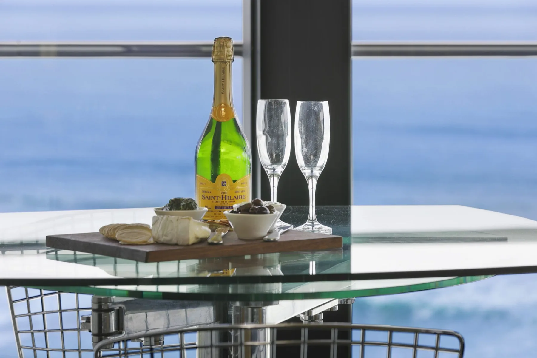 A dining table by a large window is set with champagne and glasses.
