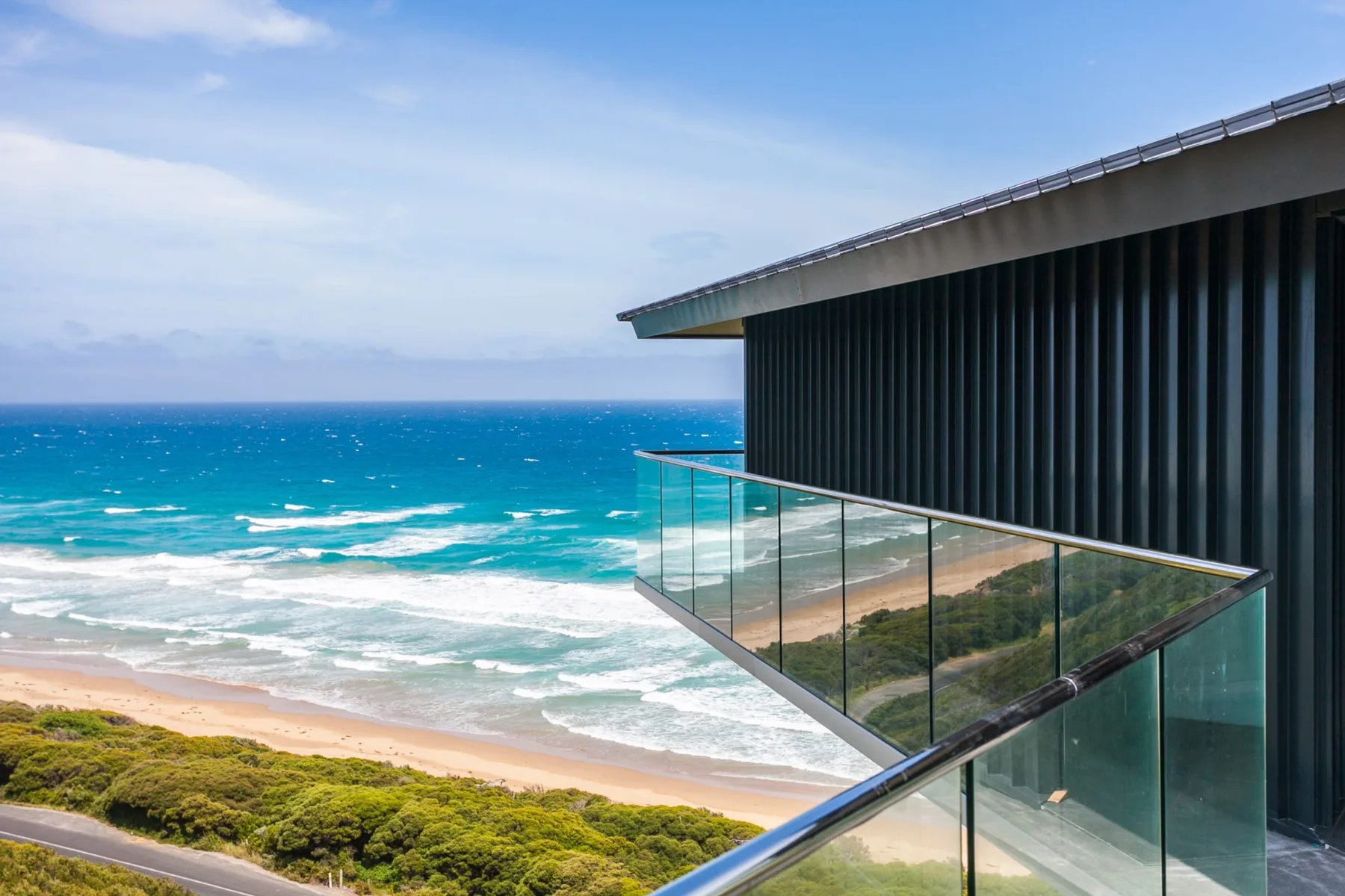 A modern house overlooks the ocean from a glass-railed balcony.