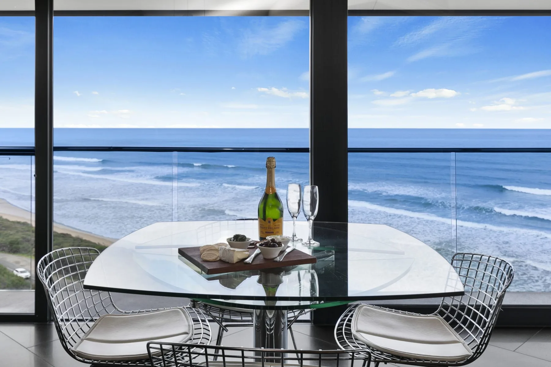 A glass dining table and seating face the ocean through large windows.