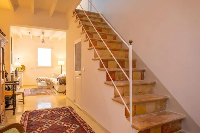 Una escalera sube junto a una sala iluminada con una alfombra estampada.