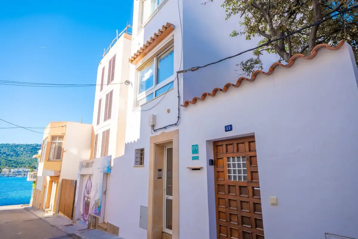 Una calle costera con fachadas blancas y el mar visible al fondo.