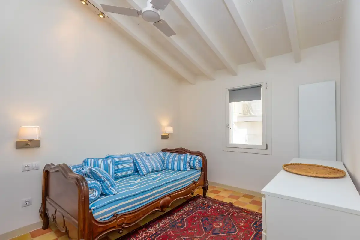 Un dormitorio luminoso con una cama de rayas azules y una alfombra estampada.