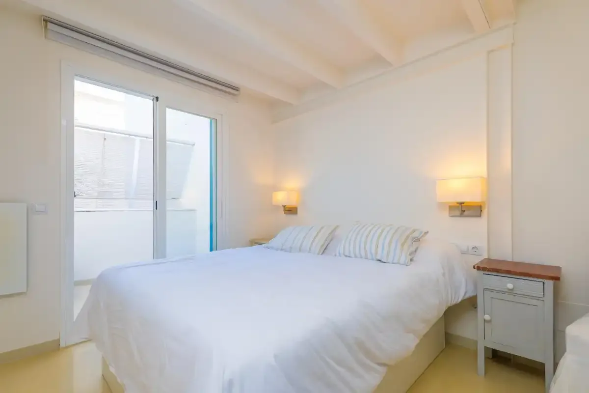 Un dormitorio luminoso con una cama blanca y puertas corredizas de vidrio.