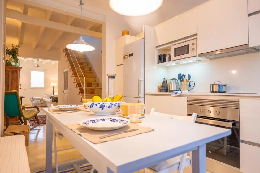 Una cocina luminosa con zona de comedor, una mesa puesta y flores.