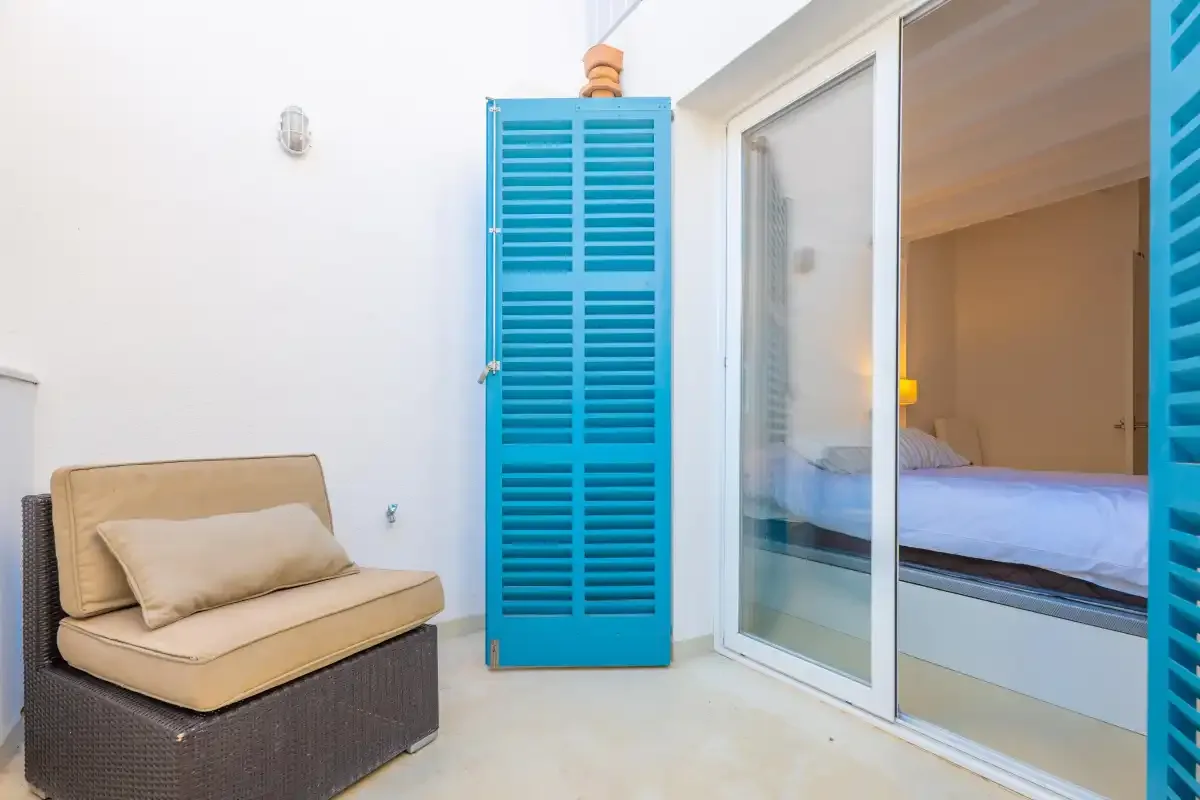 Un dormitorio luminoso da a un pequeño patio con un asiento acolchado y persianas azules.