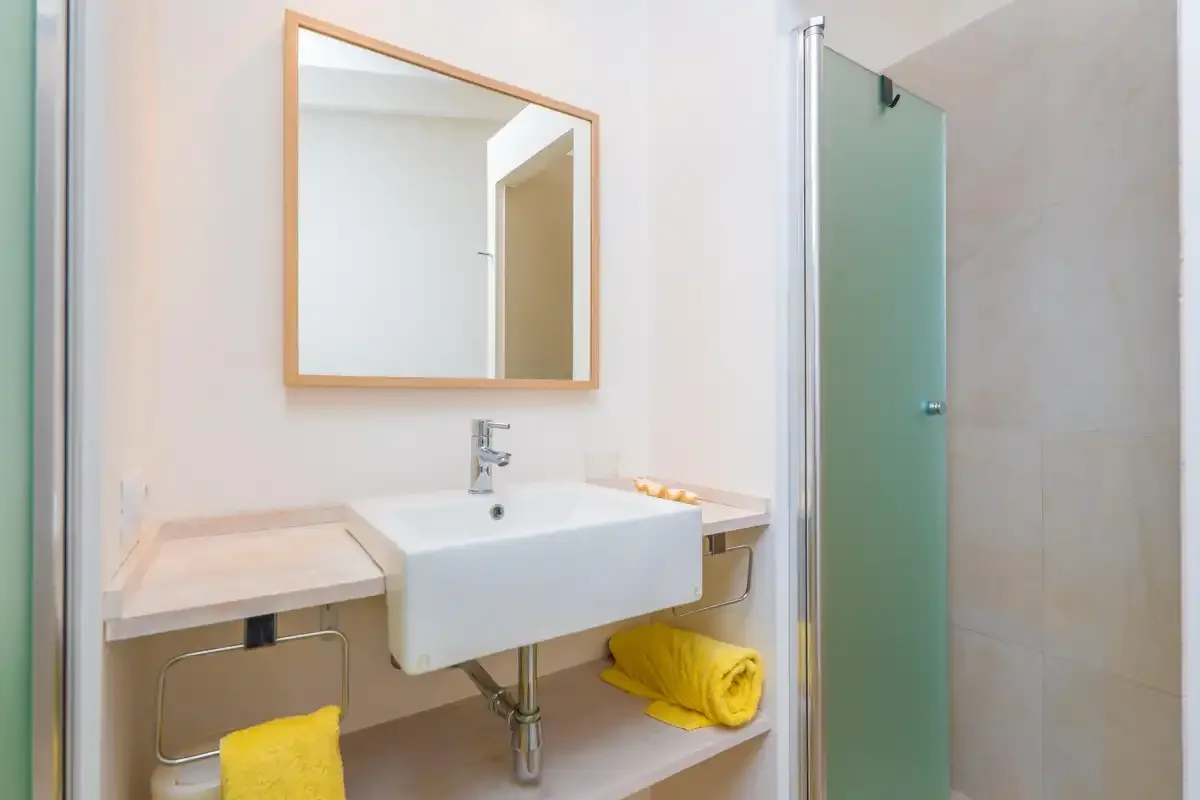 Un lavabo de baño con espejo junto a una ducha de vidrio.