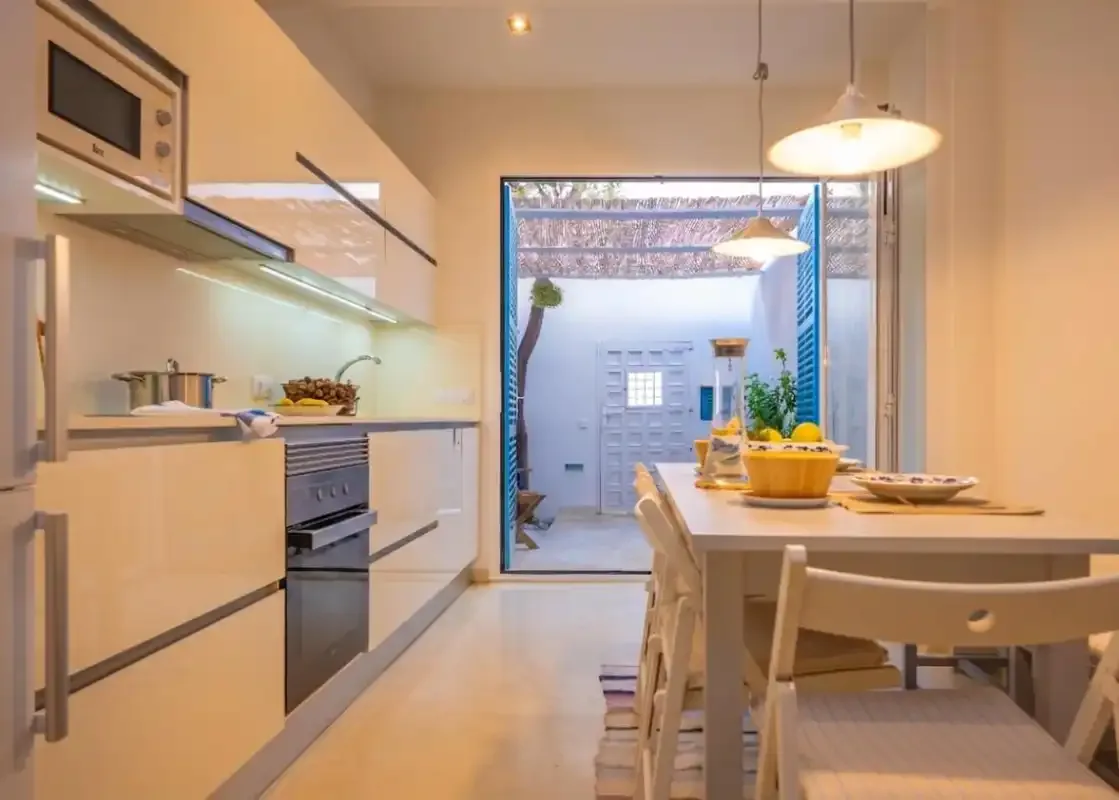 Una cocina moderna y zona de comedor con una mesa junto a una puerta abierta.