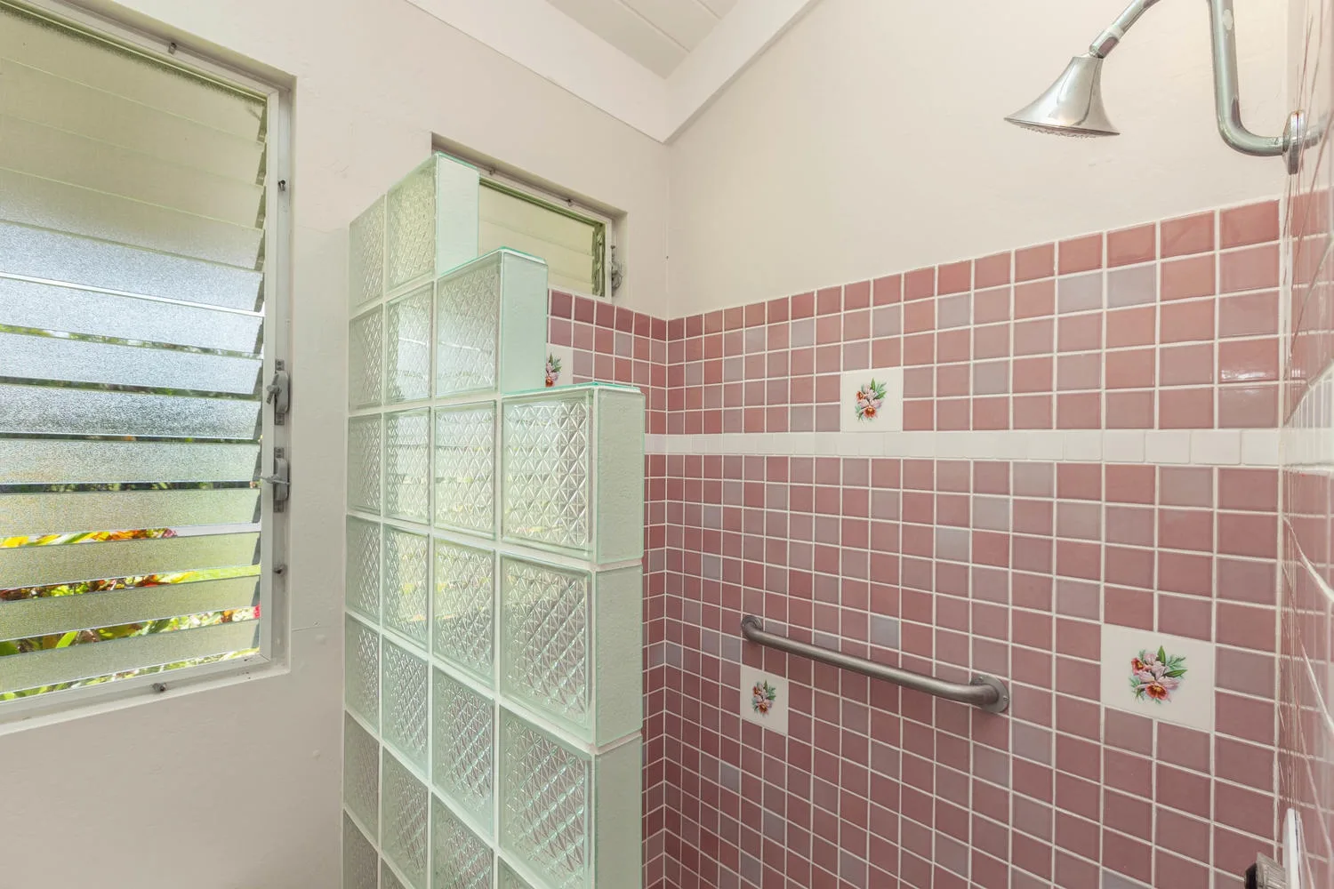 A tiled shower area has pink wall tiles and a glass-block partition.