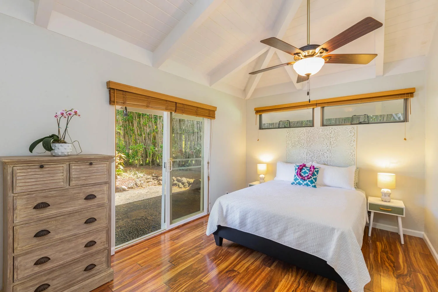 A bright bedroom with a neatly made bed and sliding glass doors opening to greenery.