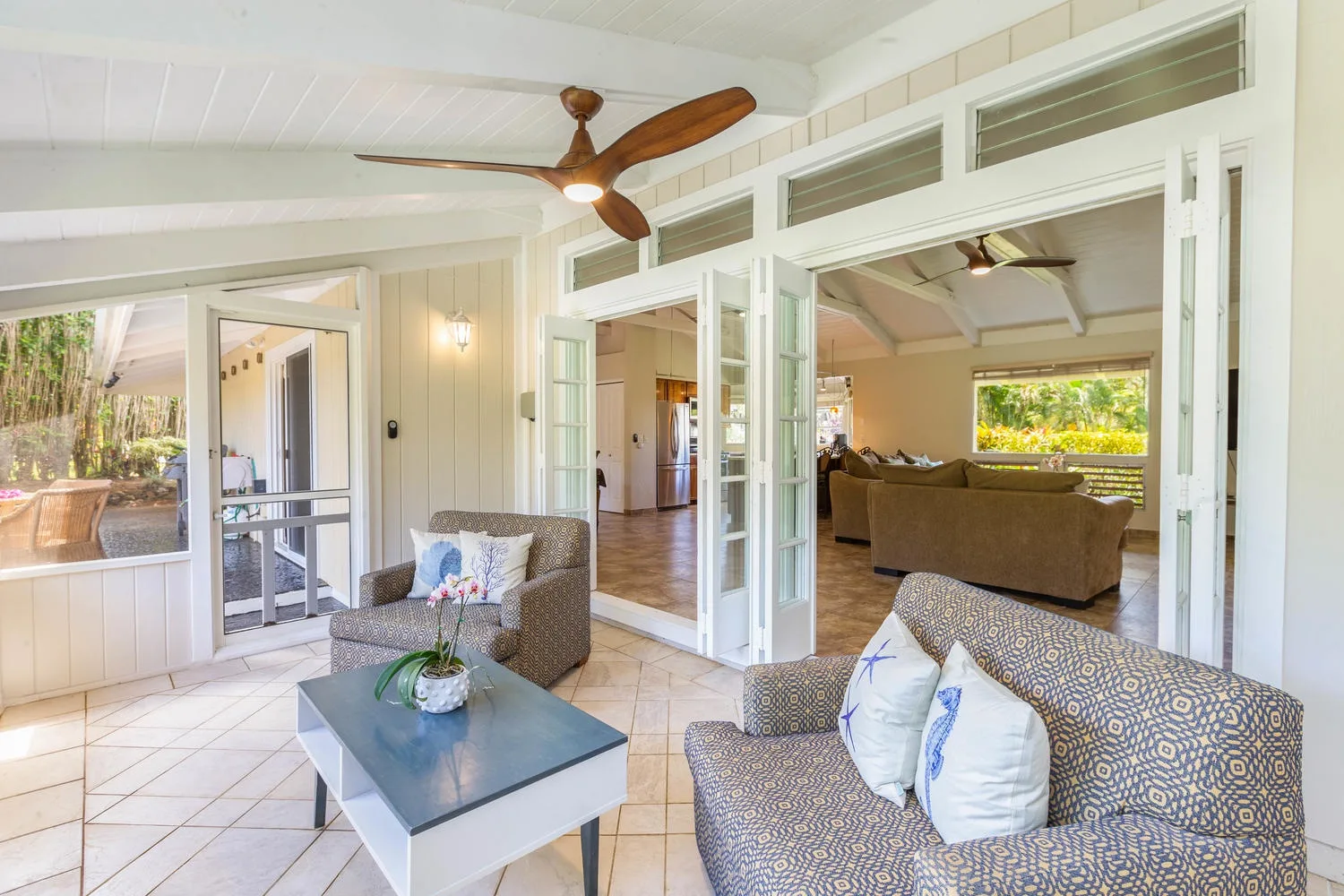 A bright living room opens through folding glass doors to another seating area.