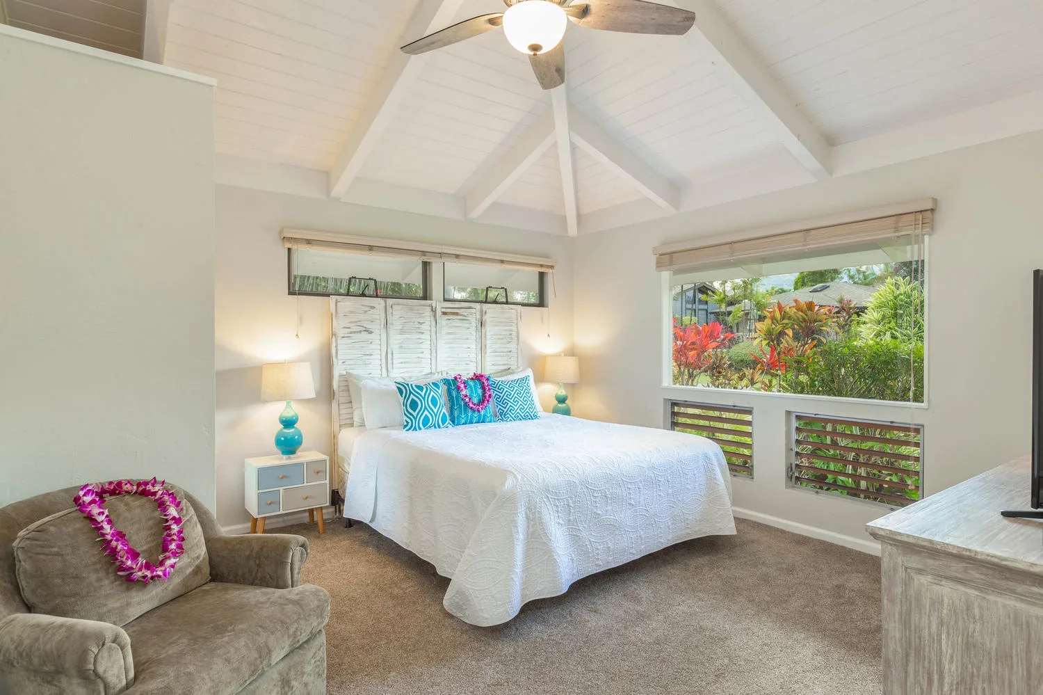 A bedroom with a bed beneath a high white ceiling and a garden view.
