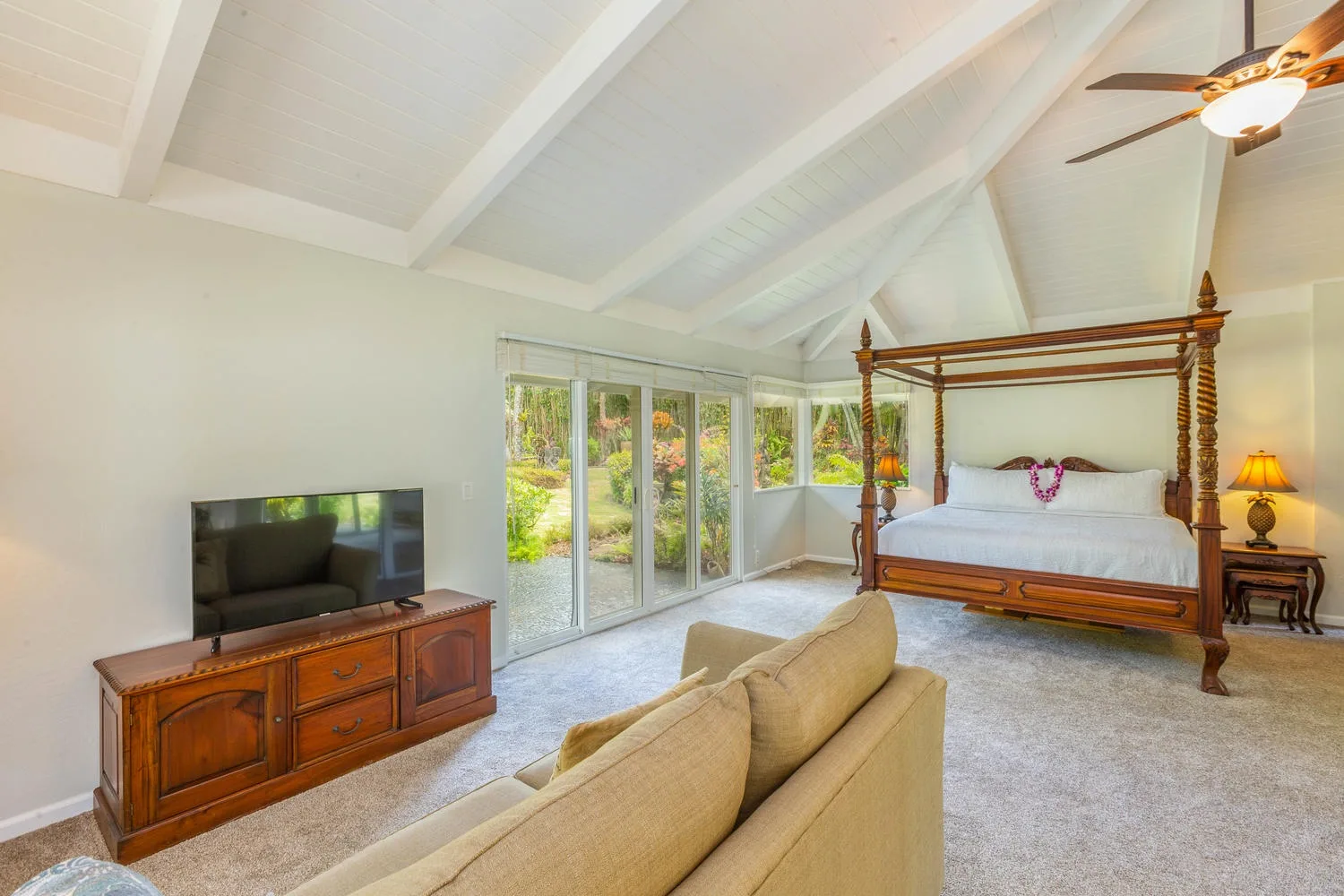 A bright bedroom with a four-poster bed, seating, and glass doors overlooking greenery.