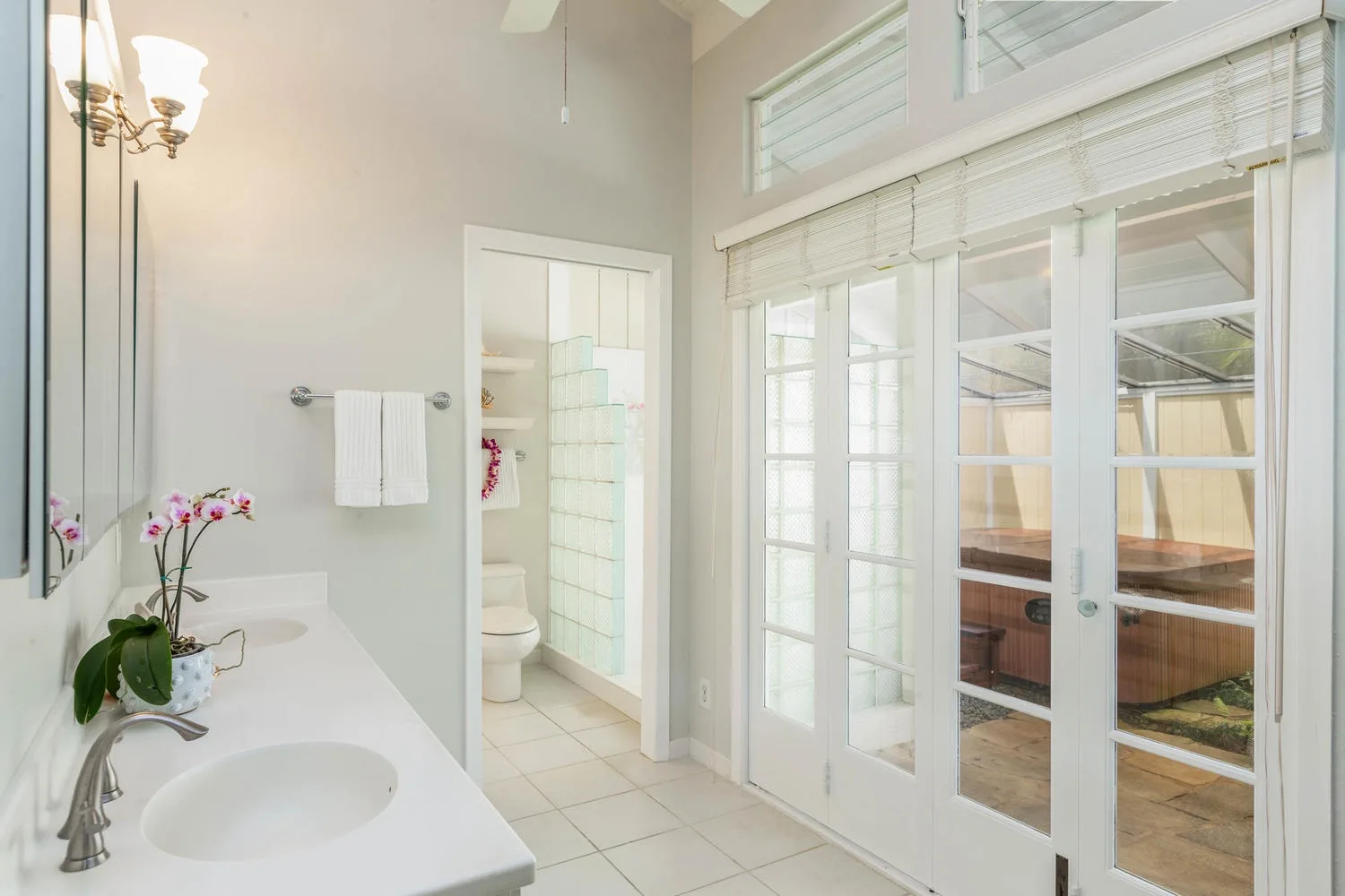 A bright bathroom with a sink, orchid, and glass doors opening to a patio.