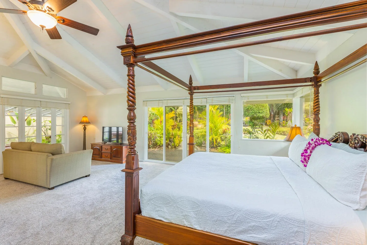 A bright bedroom with a large wooden bed and windows overlooking greenery.