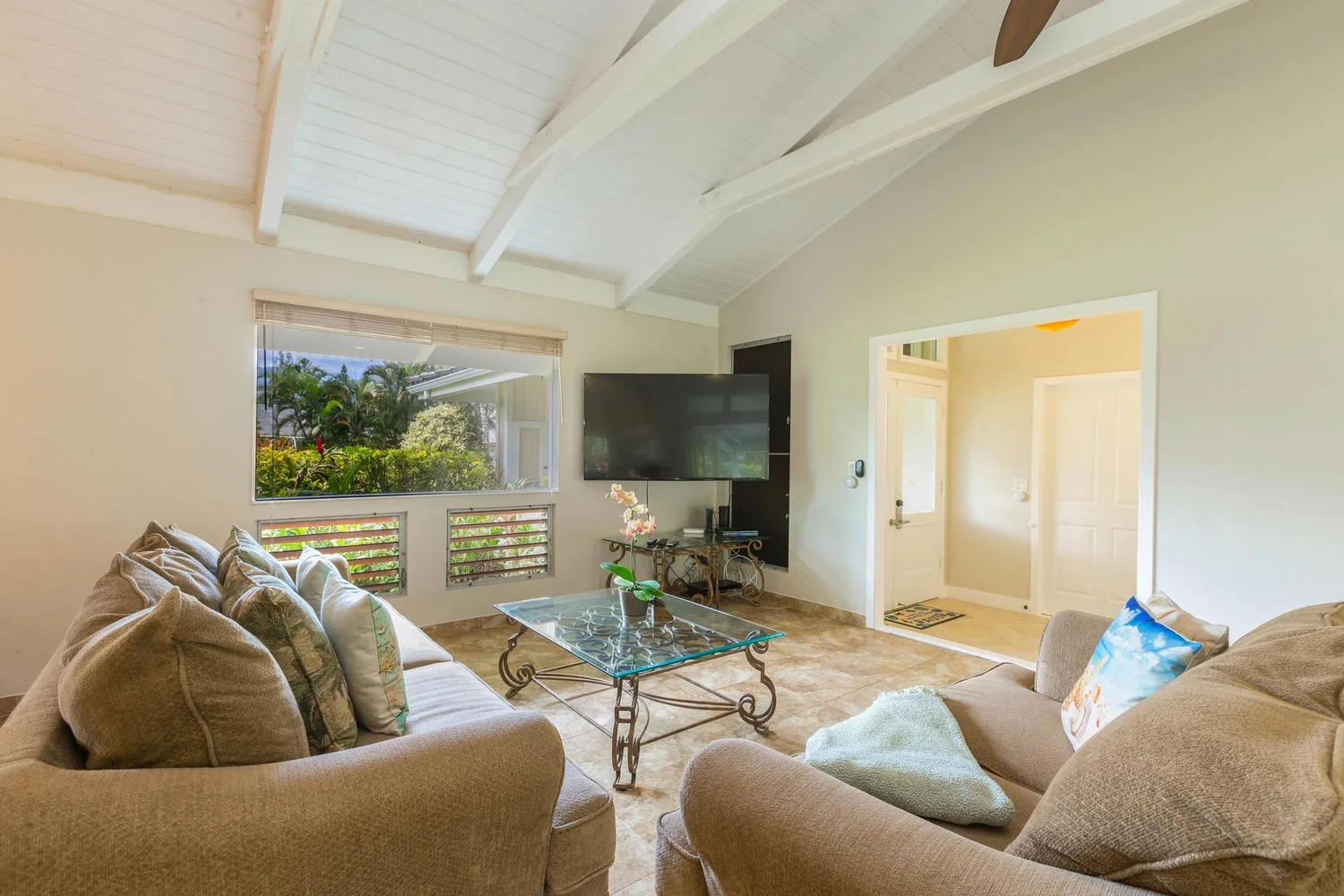 A living room with seating, a glass coffee table, and a television.