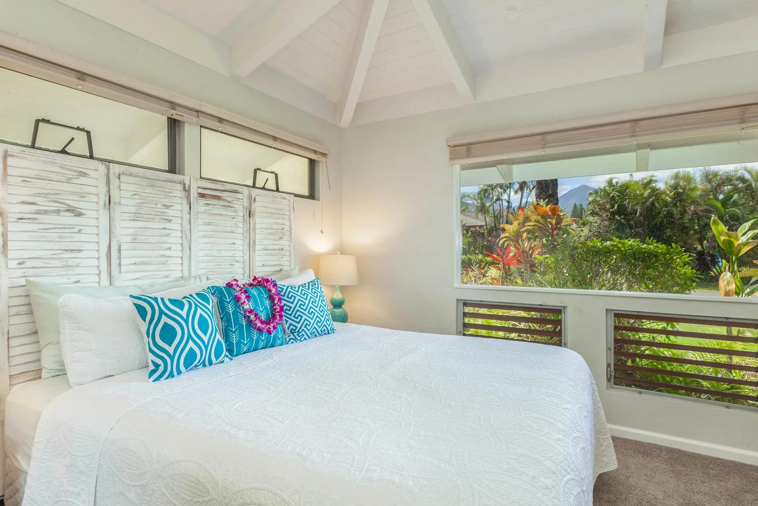 A bright bedroom with a neatly made bed beside a wide window overlooking greenery.