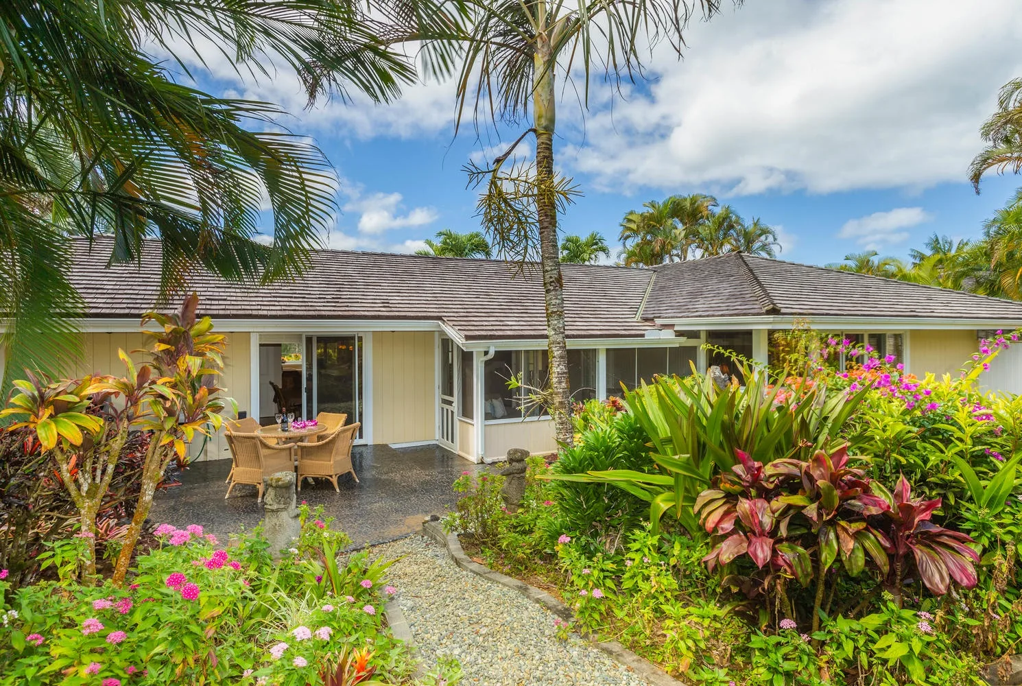 A single-story house with an outdoor dining area surrounded by tropical plants and flowers.