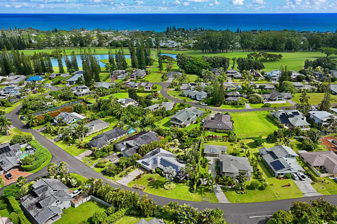 An aerial view of a residential neighborhood with green lawns and the ocean beyond.