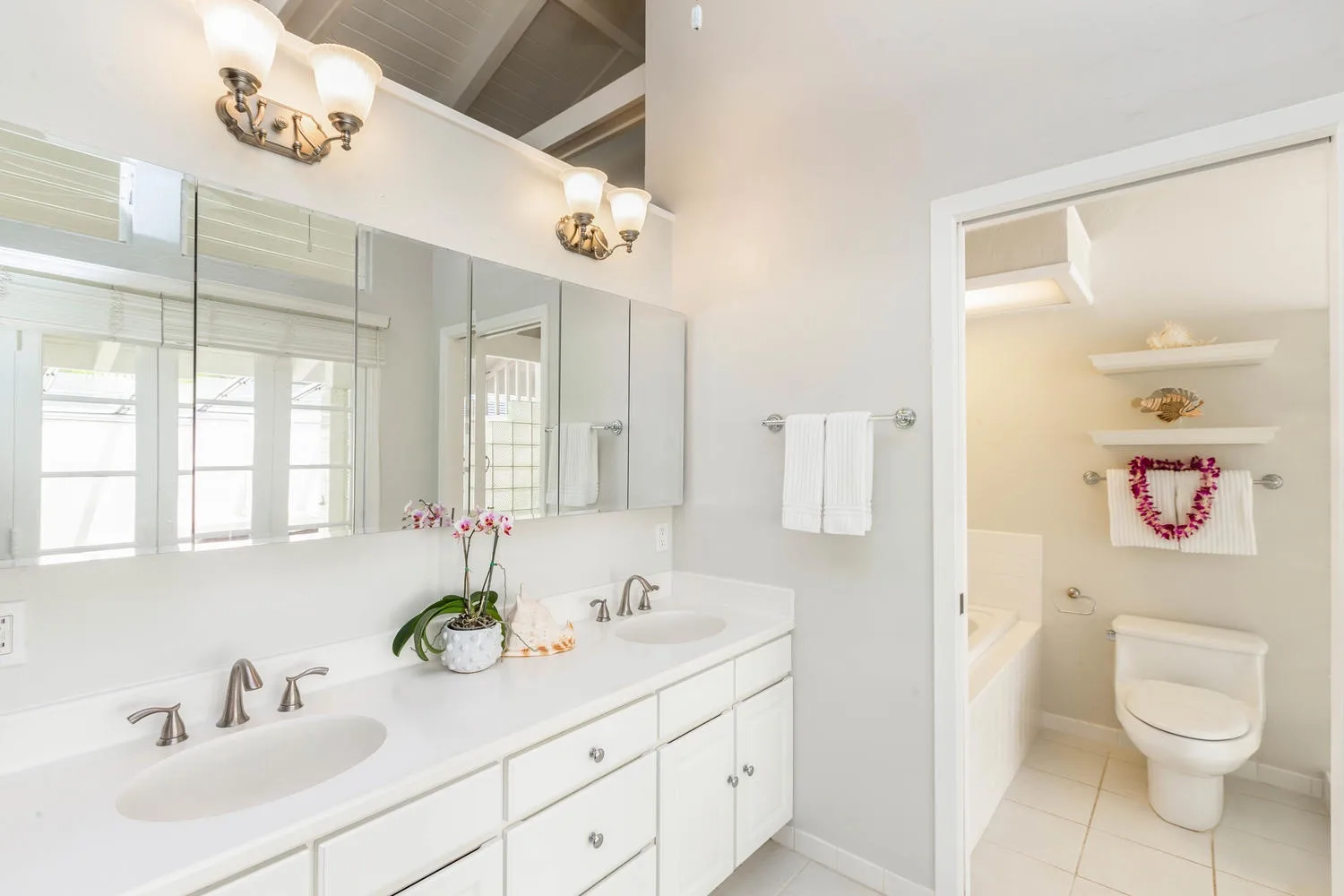 A bright bathroom with a double sink vanity and an adjoining toilet area.