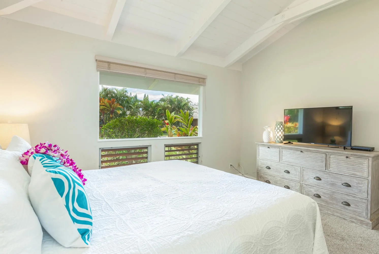 A bright bedroom with a bed, colorful pillows, and a television on a dresser.