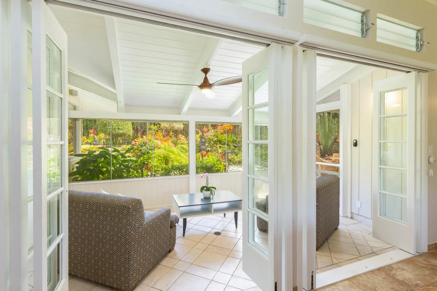 A bright enclosed sitting area opens onto a garden, with tiled flooring and glass doors.