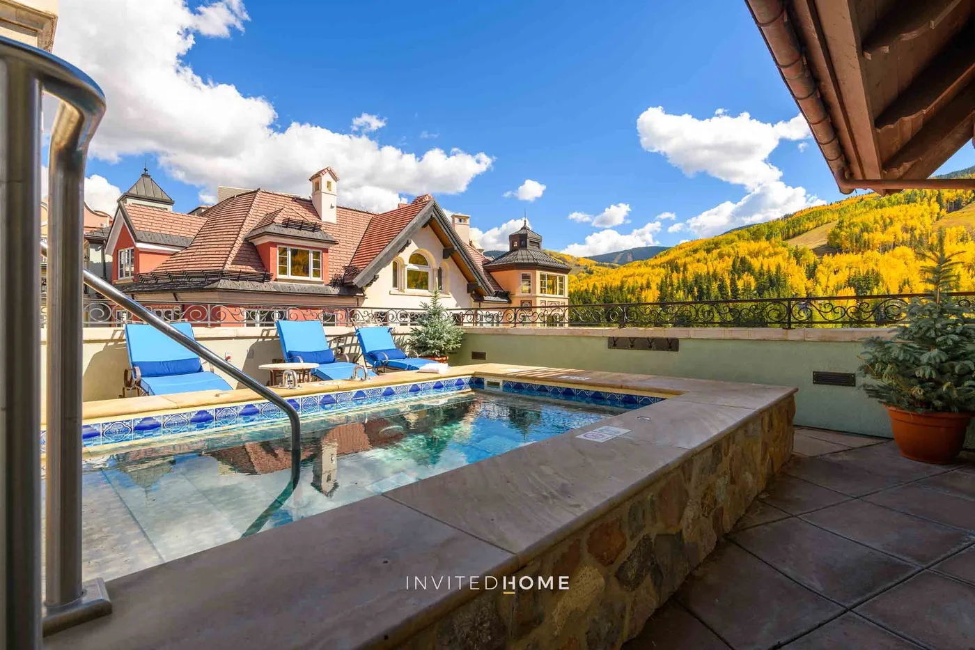 Una piscina exterior tiene vistas a edificios cercanos y una ladera arbolada.