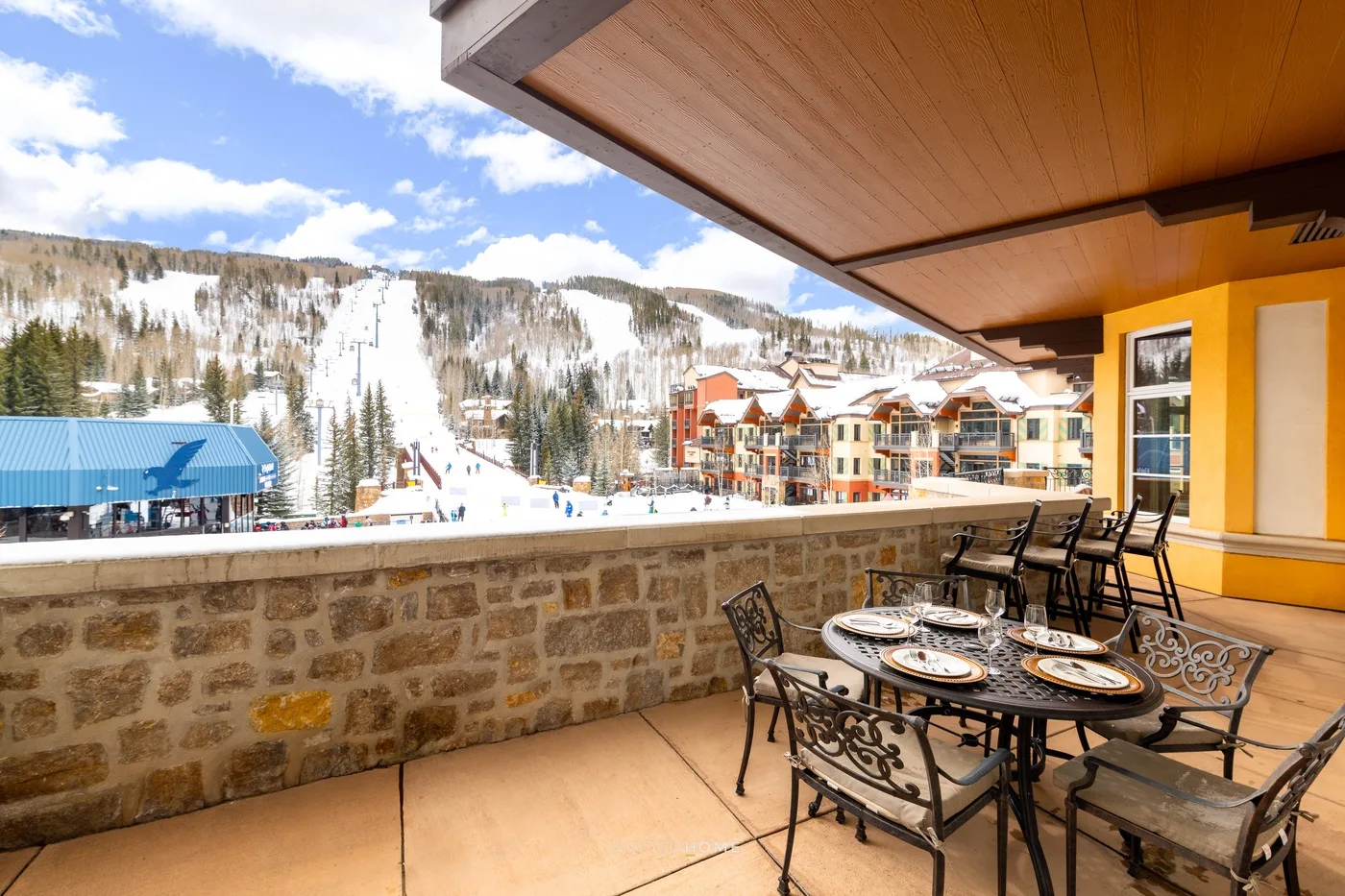 Una terraza exterior con comedor mira hacia pistas nevadas y edificios cercanos.