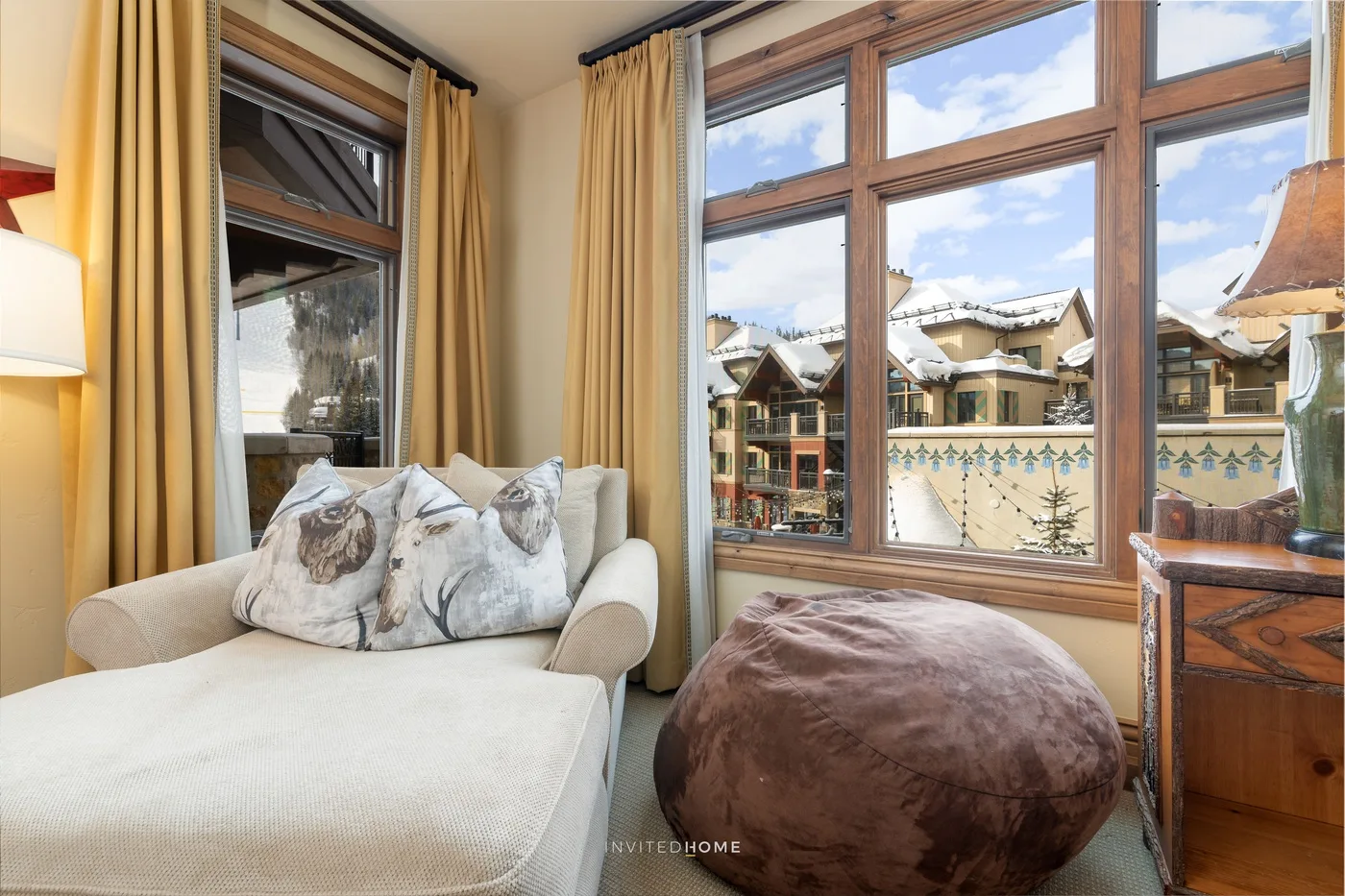 Una luminosa zona de estar con un asiento acolchado junto a grandes ventanas con vistas a edificios cercanos.