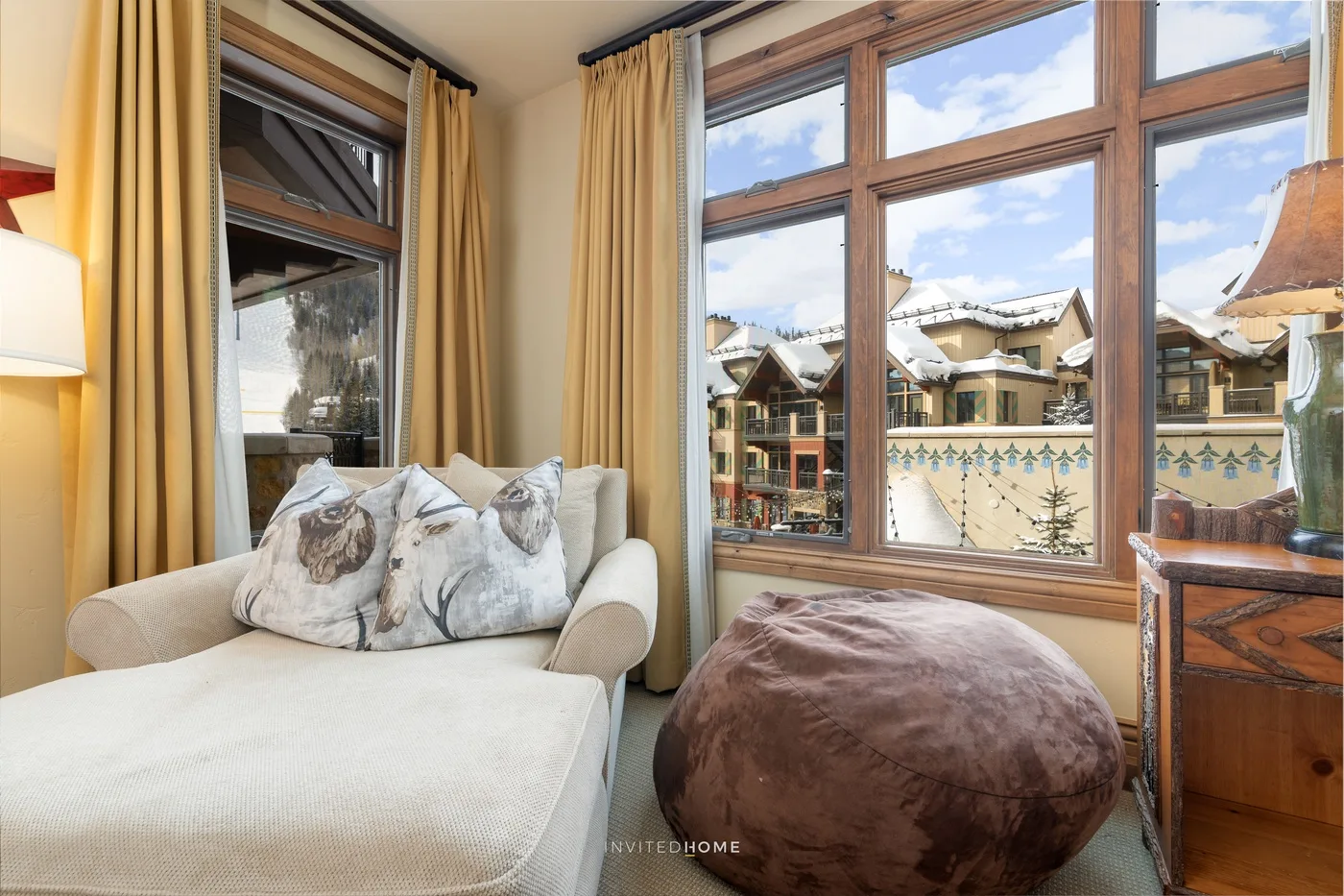 Una luminosa zona de estar cuenta con una chaise longue color crema junto a grandes ventanas con marcos de madera.