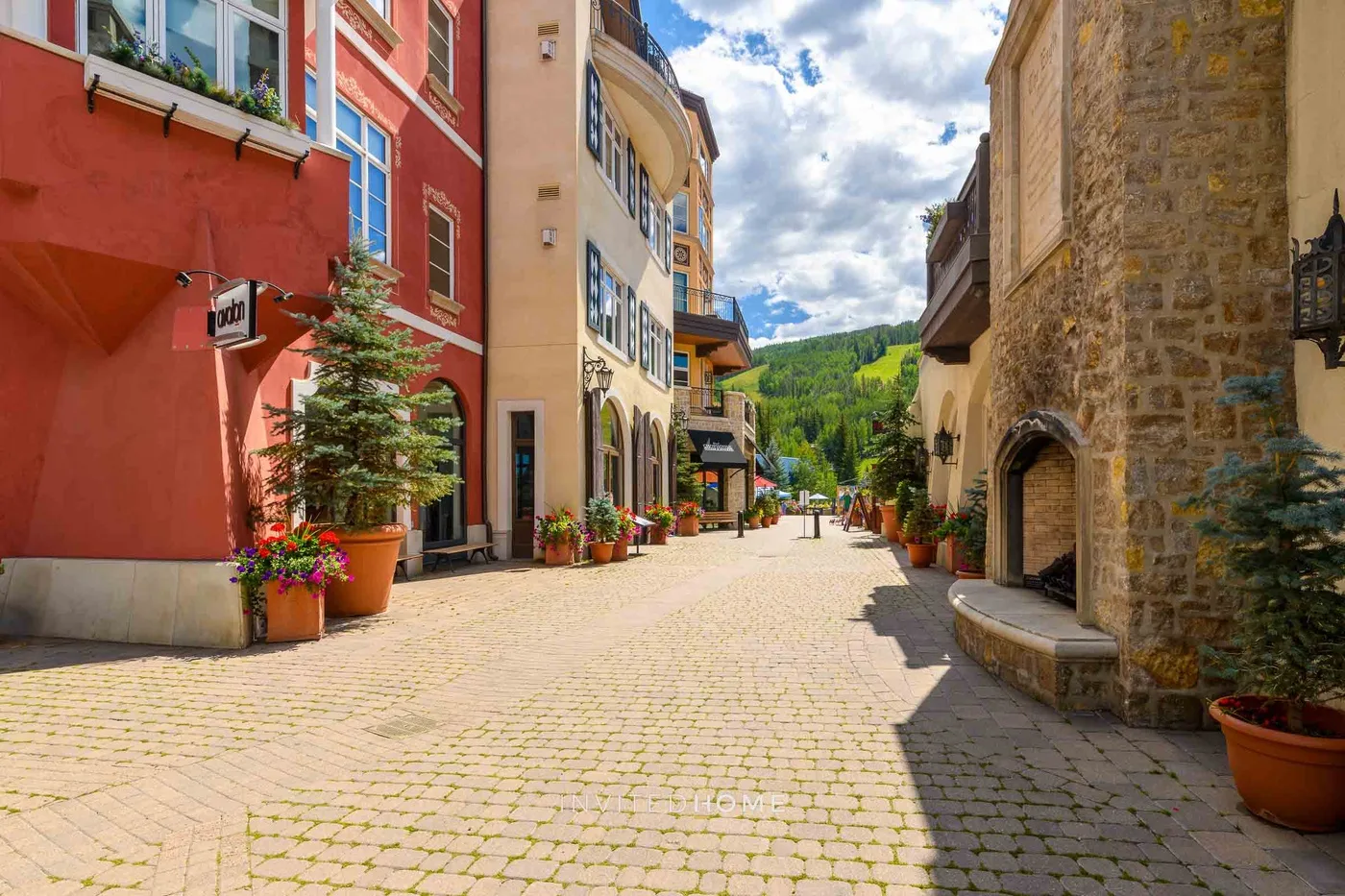 Una calle peatonal adoquinada pasa entre edificios coloridos, con colinas verdes al fondo.