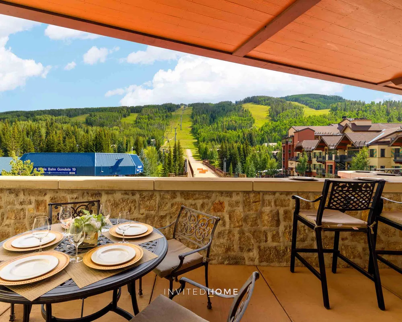 Una terraza cubierta mira hacia colinas verdes, con una mesa de comedor y asientos en primer plano.