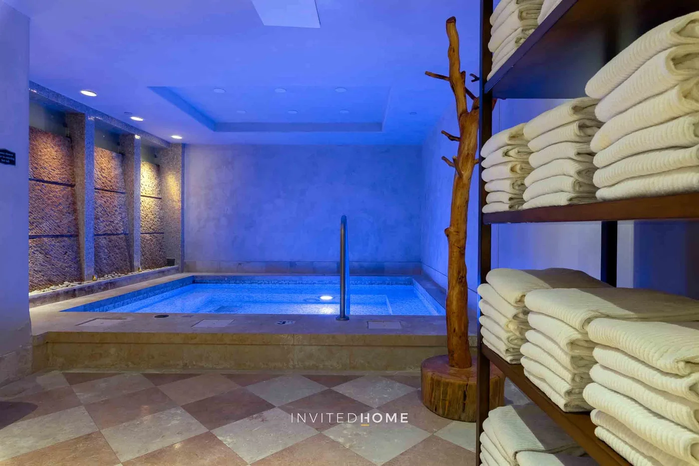 Una piscina interior está junto a estantes con toallas dobladas.