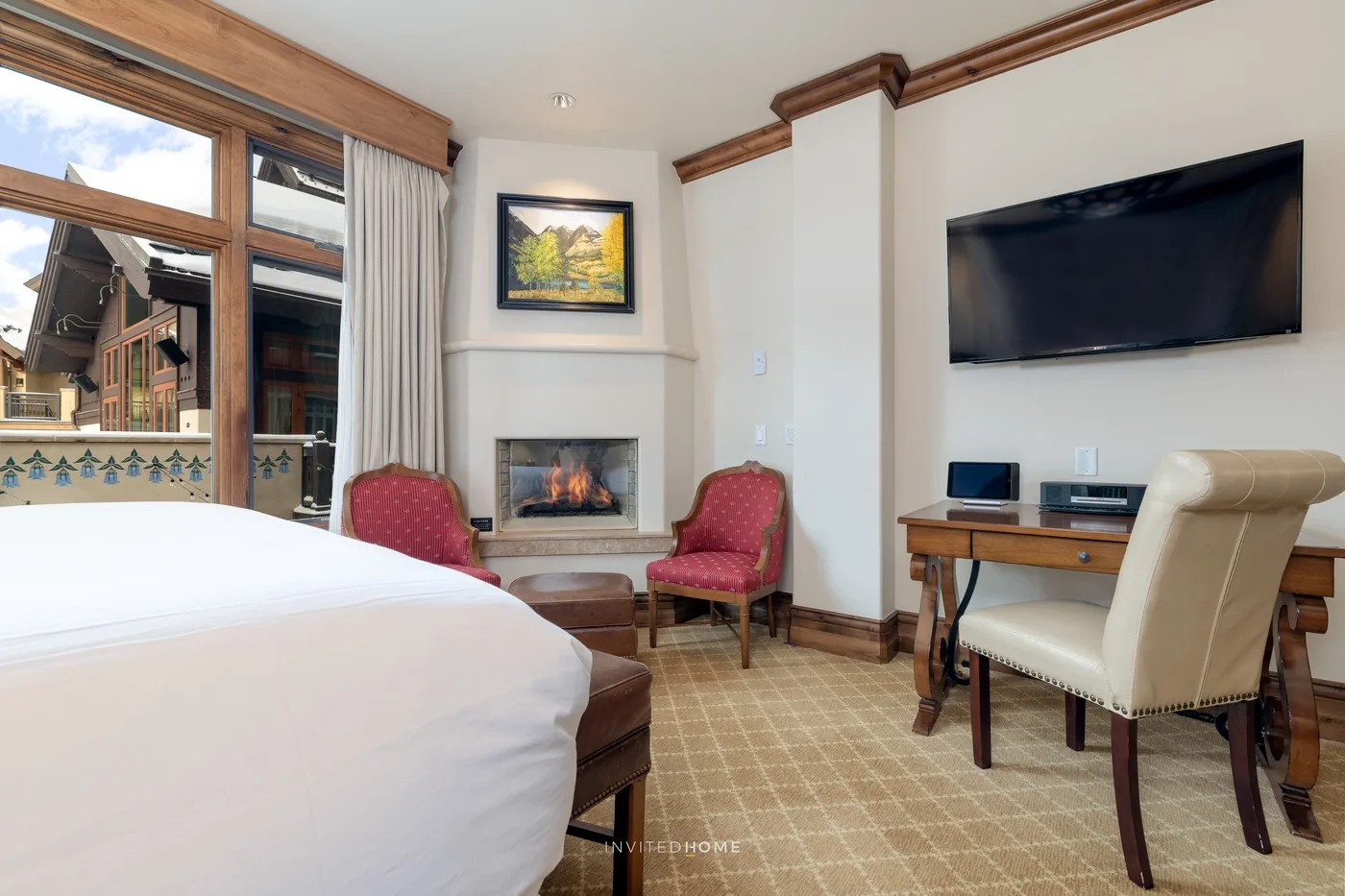 Zona de estar de un dormitorio con cama, chimenea y televisor en la pared.