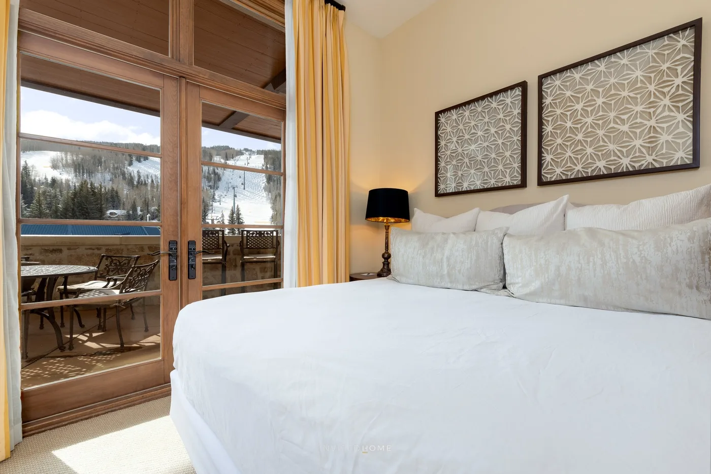 Dormitorio con una cama tendida junto a puertas de vidrio que dan a un balcón.