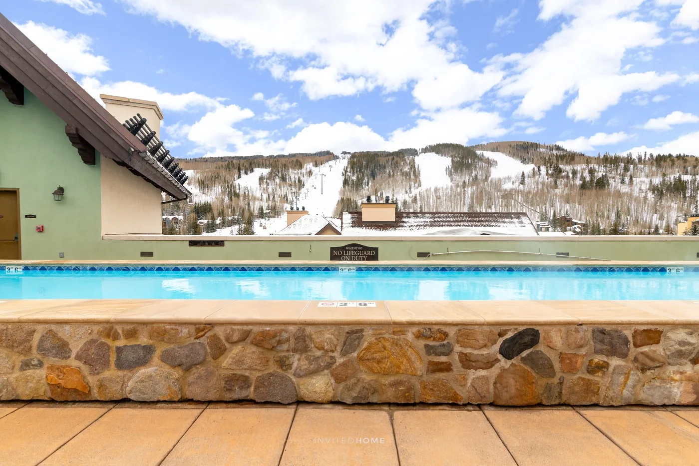 Una piscina al aire libre ofrece vistas a montañas nevadas bajo un cielo parcialmente nublado.