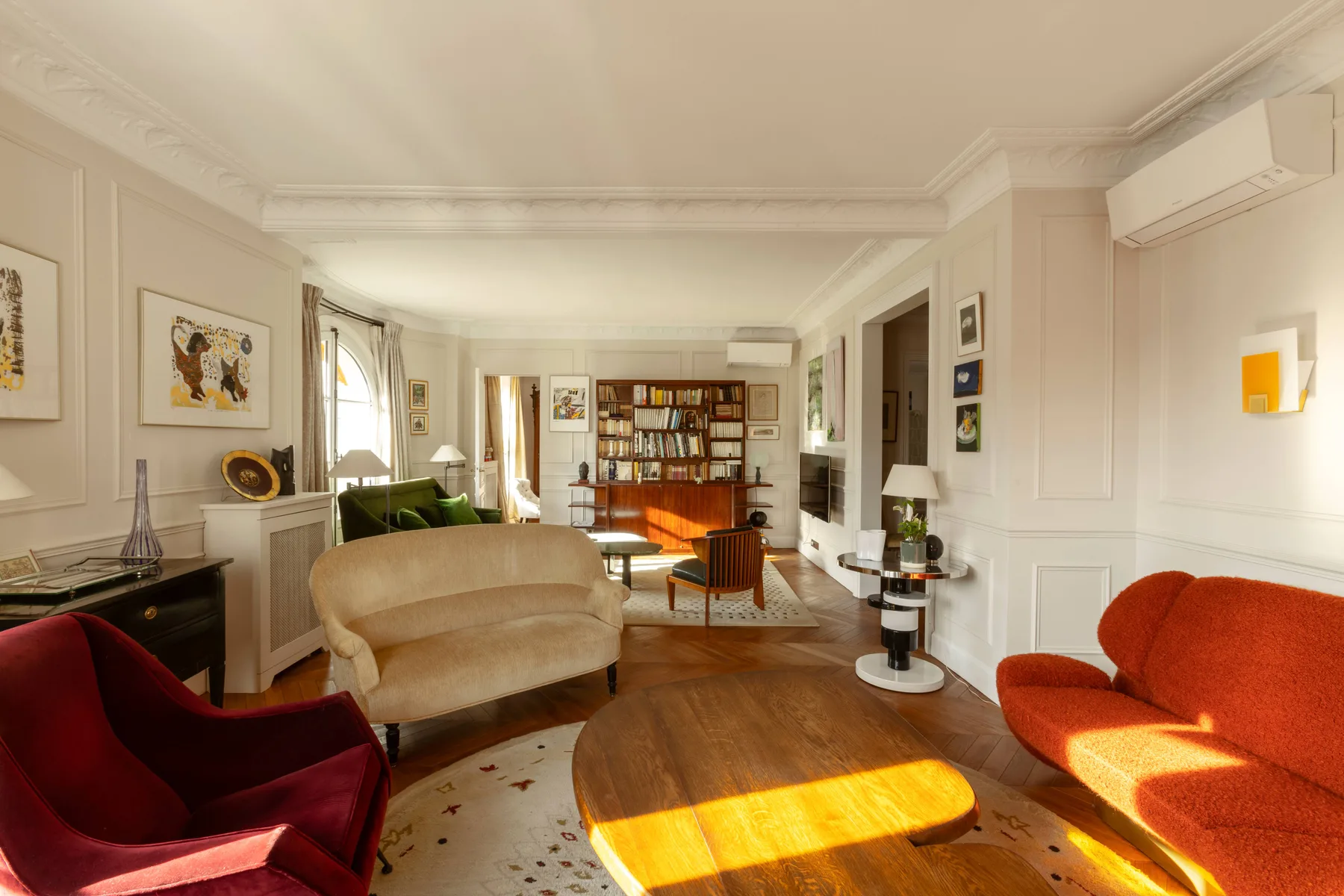 Una sala de estar luminosa con varios asientos y una estantería al fondo.