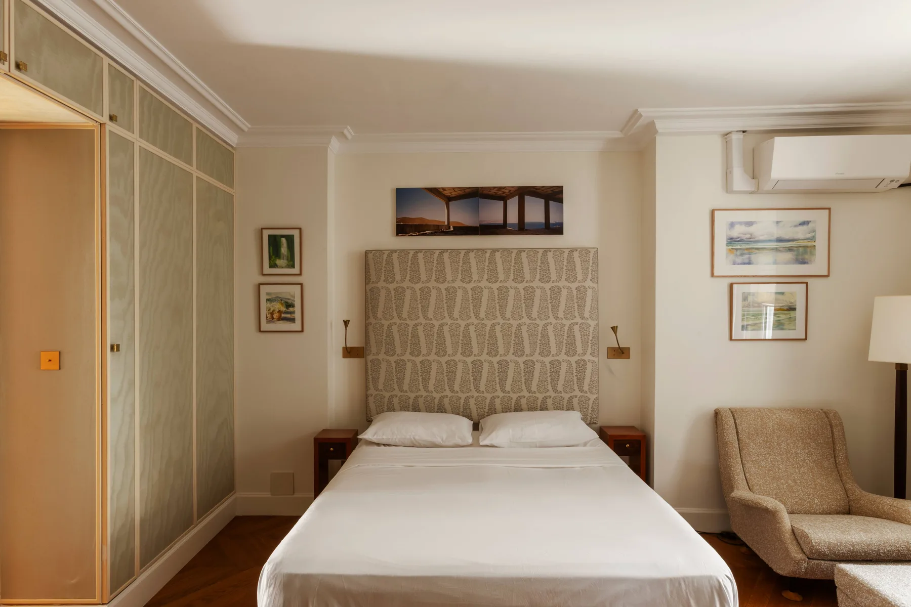 Un dormitorio con una cama bien tendida y un cabecero tapizado.