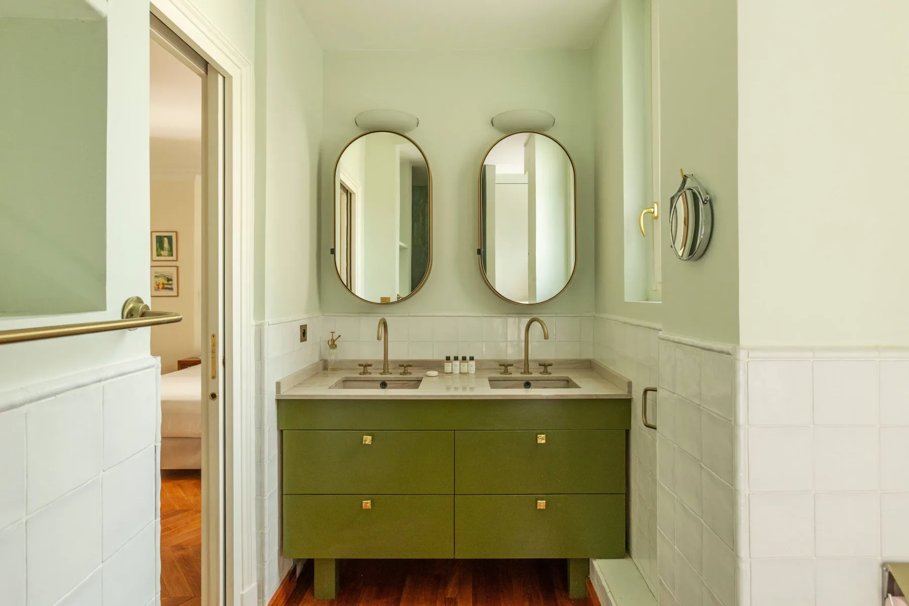 A bathroom vanity with a green cabinet, two mirrors, and wall-mounted lights.