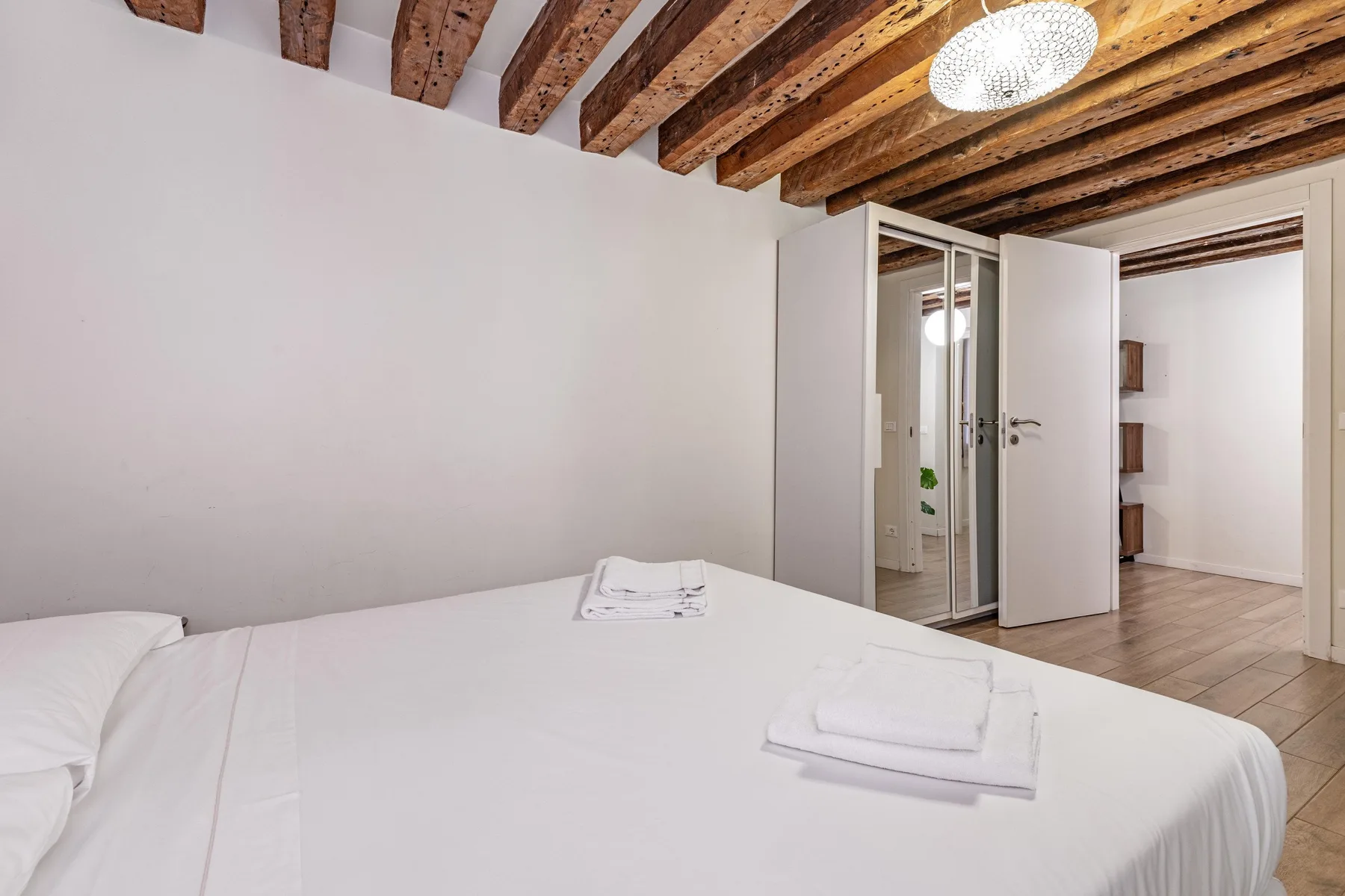 A bedroom with a neatly made bed and exposed wooden ceiling beams.