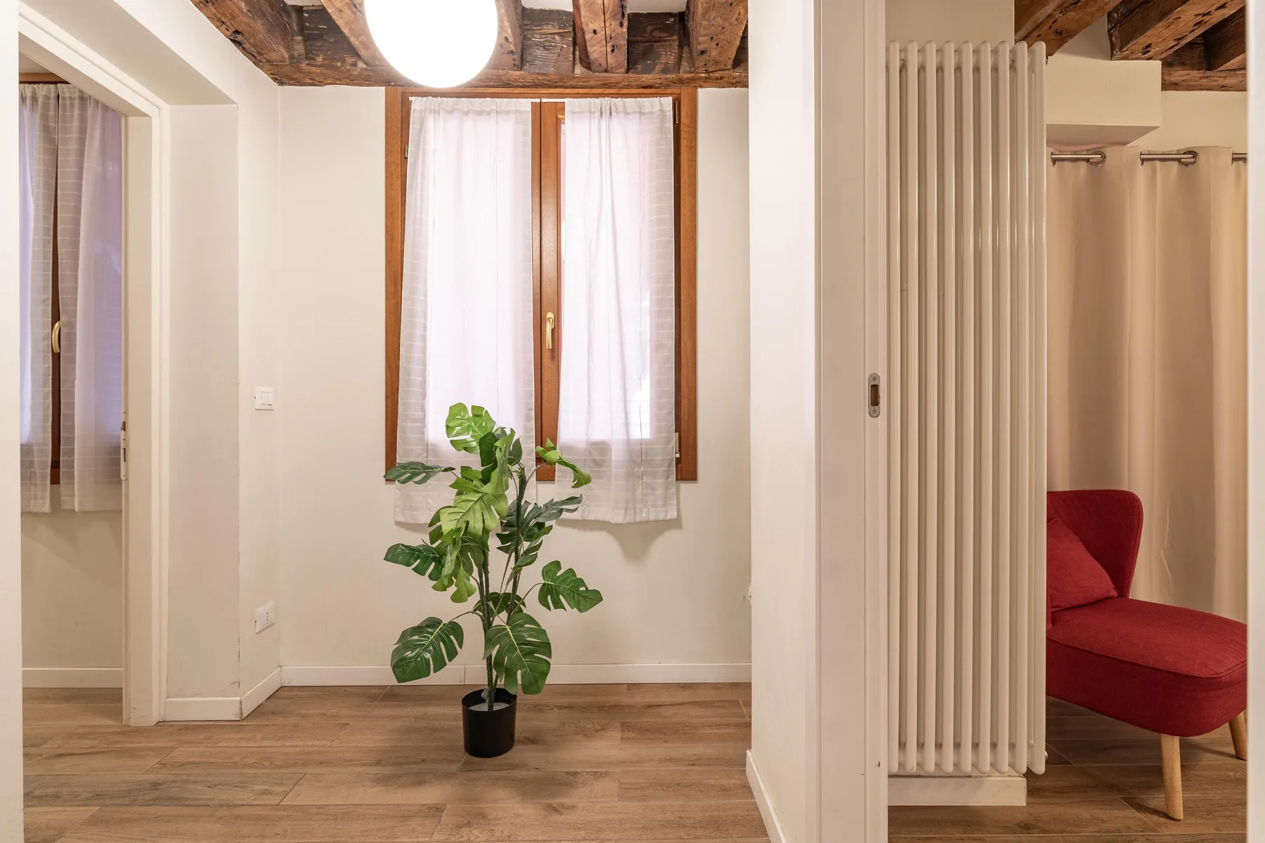 A bright interior hallway with a potted plant beneath a curtained window.