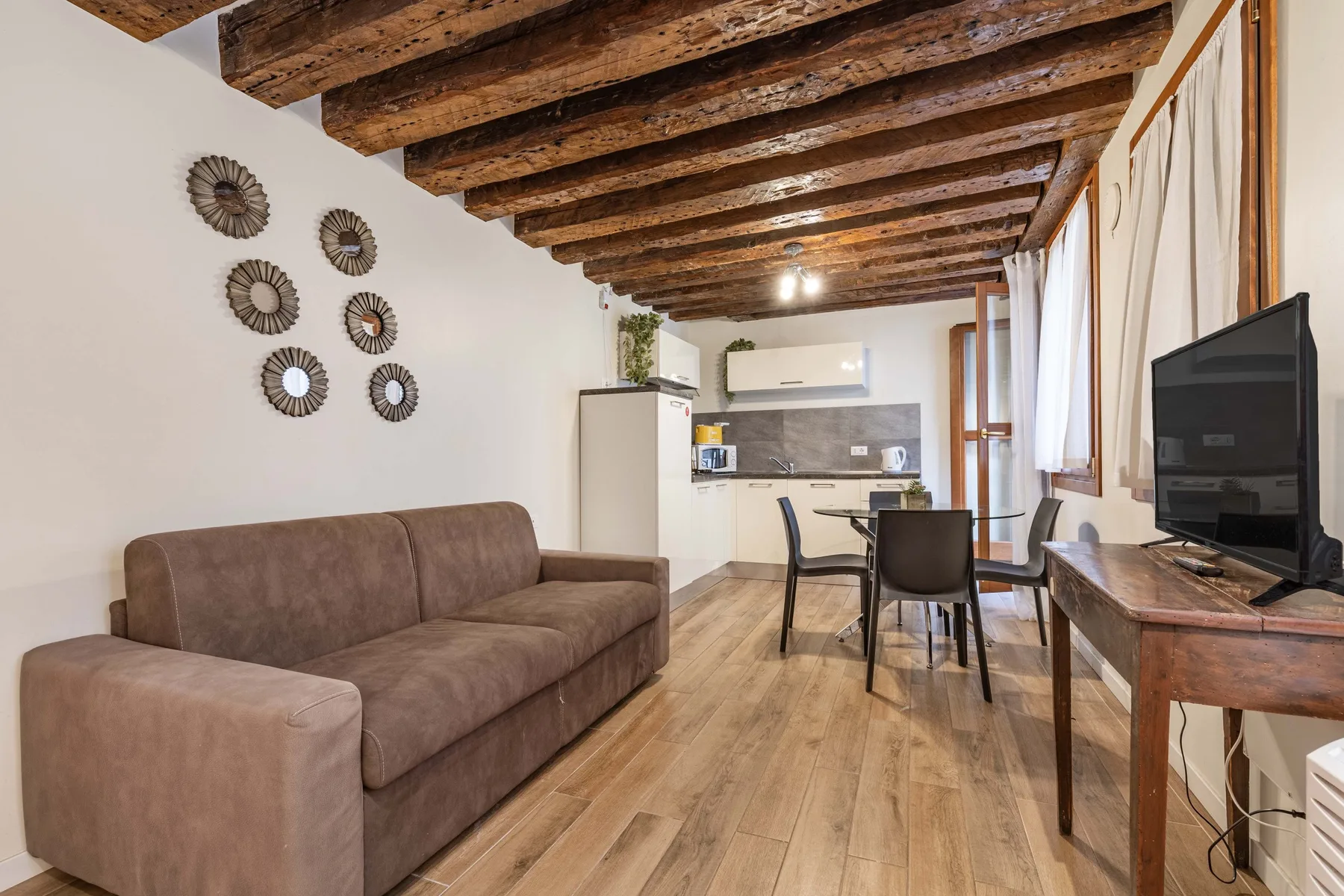 A living room with seating, a television, and a dining area beneath exposed wooden beams.