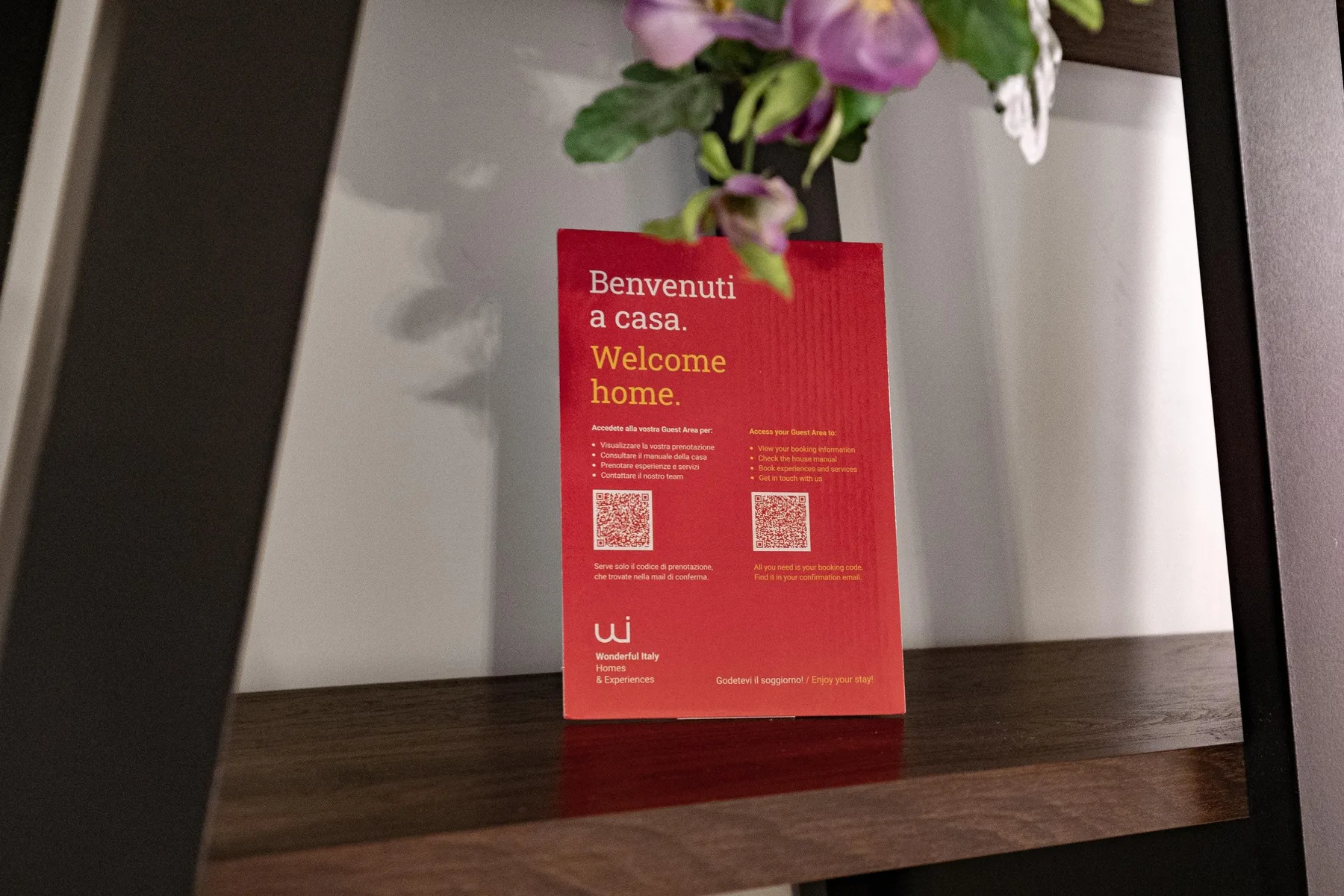 A red welcome card sits beneath flowers on a dark wooden shelf.